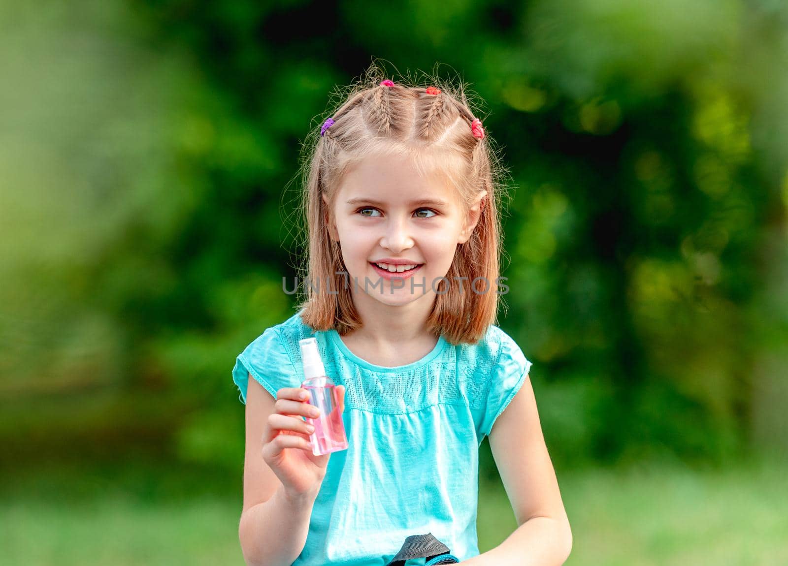 Portrait of school girl in mask holding sanitizer on nature background