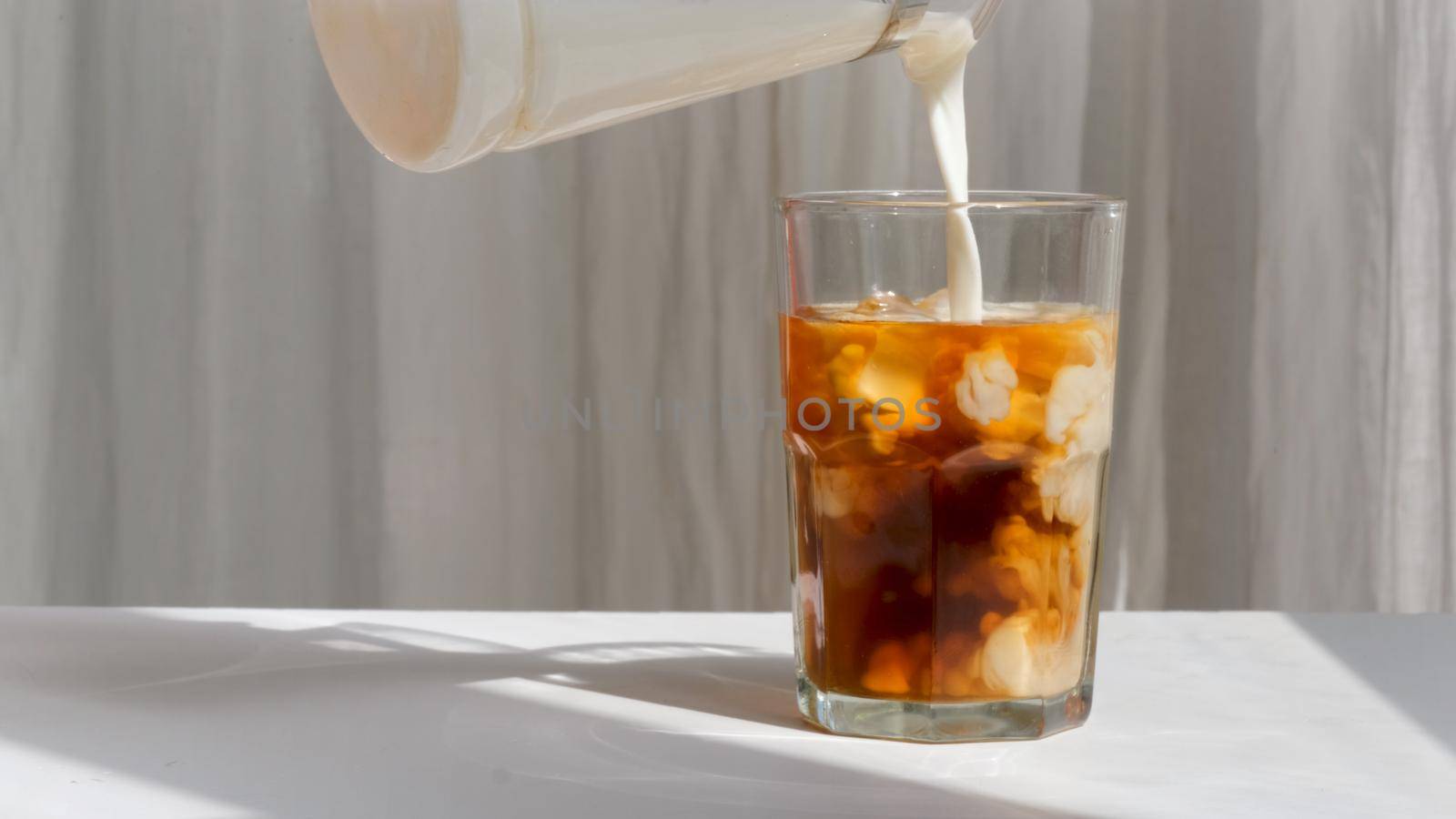Milk cream is poured into a iced coffee. Coffee cold drink with ice and milk by Demkat