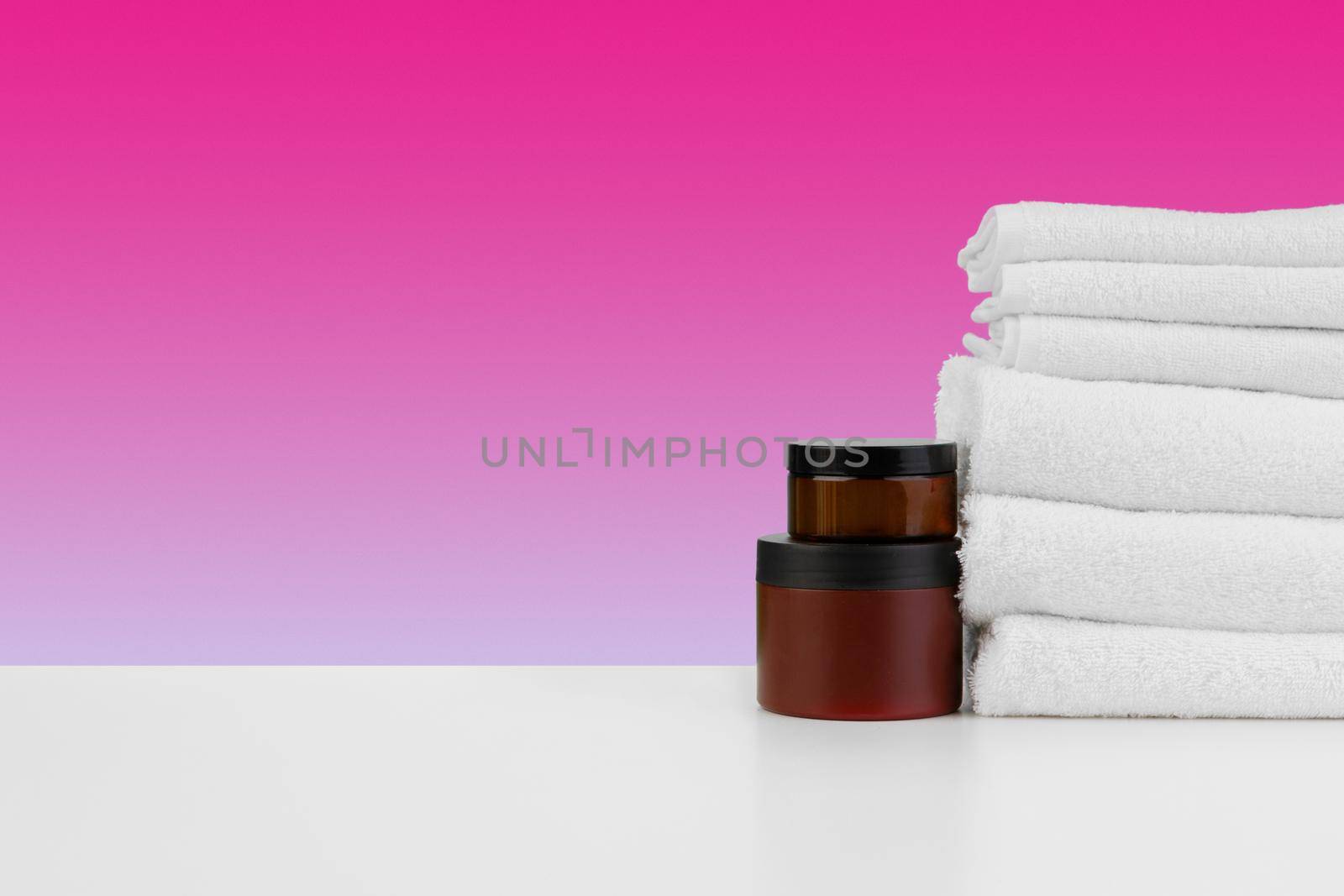 Pile of towels, bottles with shampoo on white table isolated