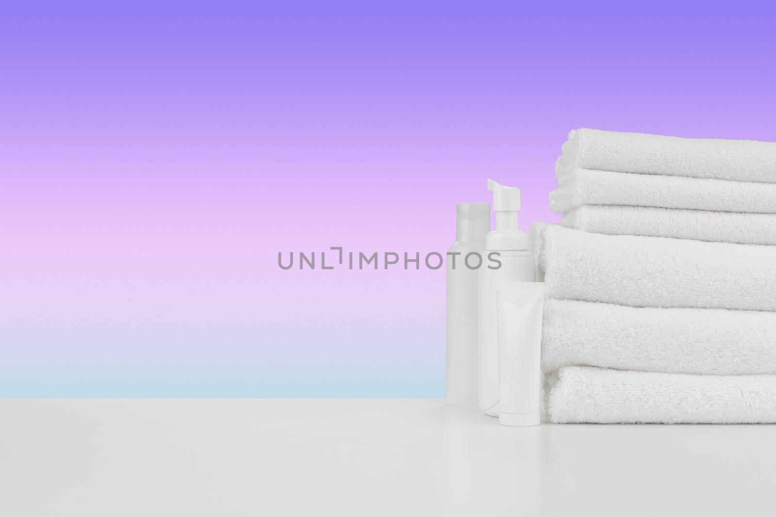 Pile of towels, bottles with shampoo on white table isolated
