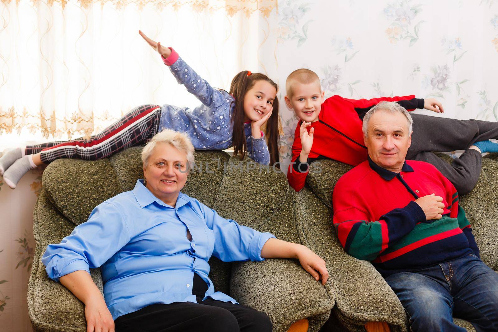 Happy young boy and girl with their laughing grandparents smiling at the camera as they pose together indoors by Andelov13