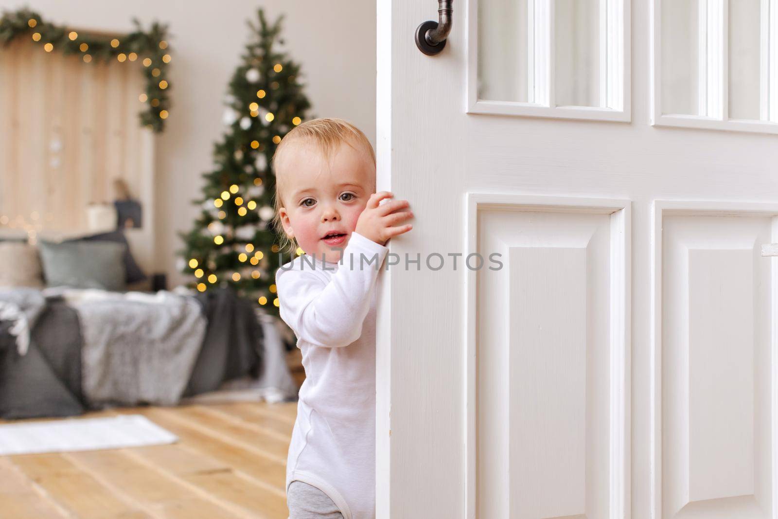 Baby boy peeking out of the open white room door
