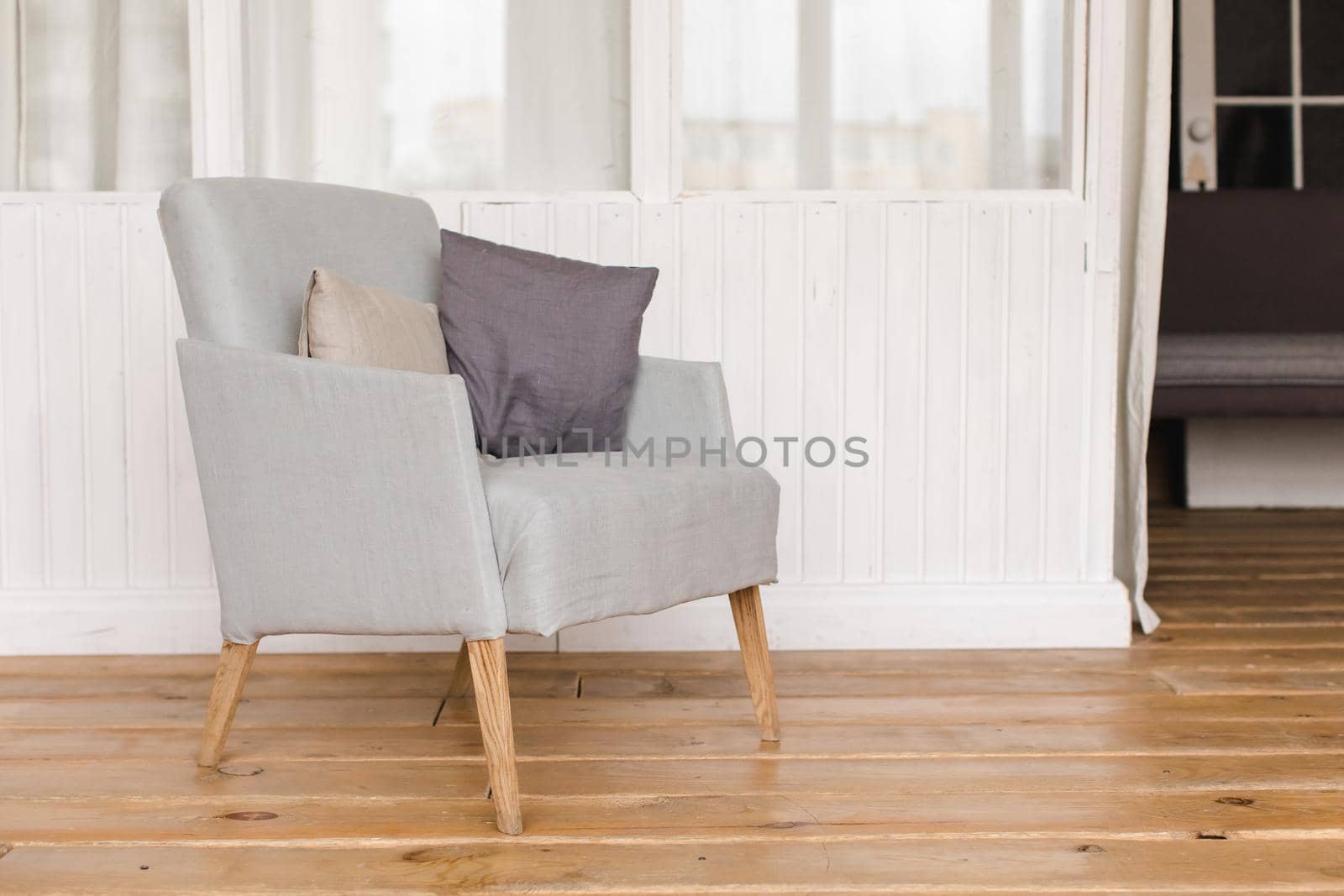 Interior shot of simple comfortable armchair with cushions on wooden floor
