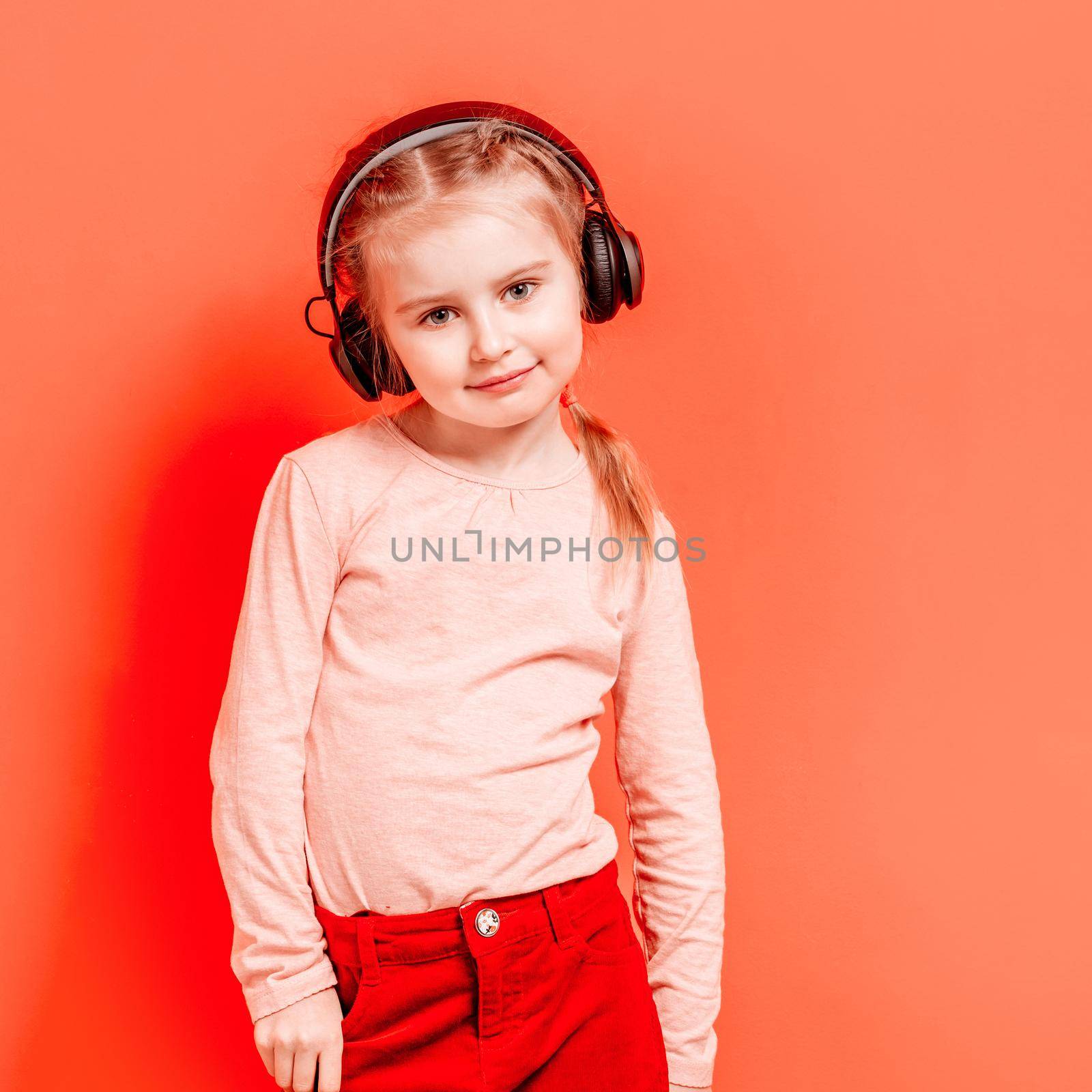 Modern little girl posing in headphones over rose background