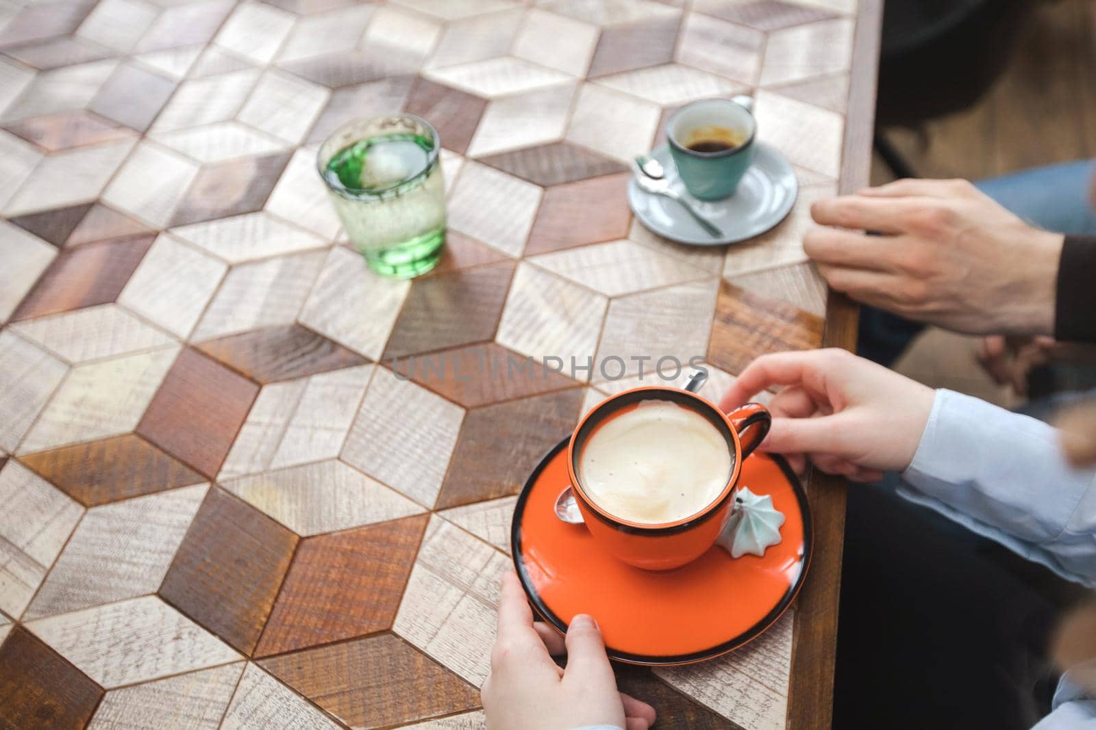 From above crop shot of man and woman having cups of coffee sitting at table with ornamental wood desk