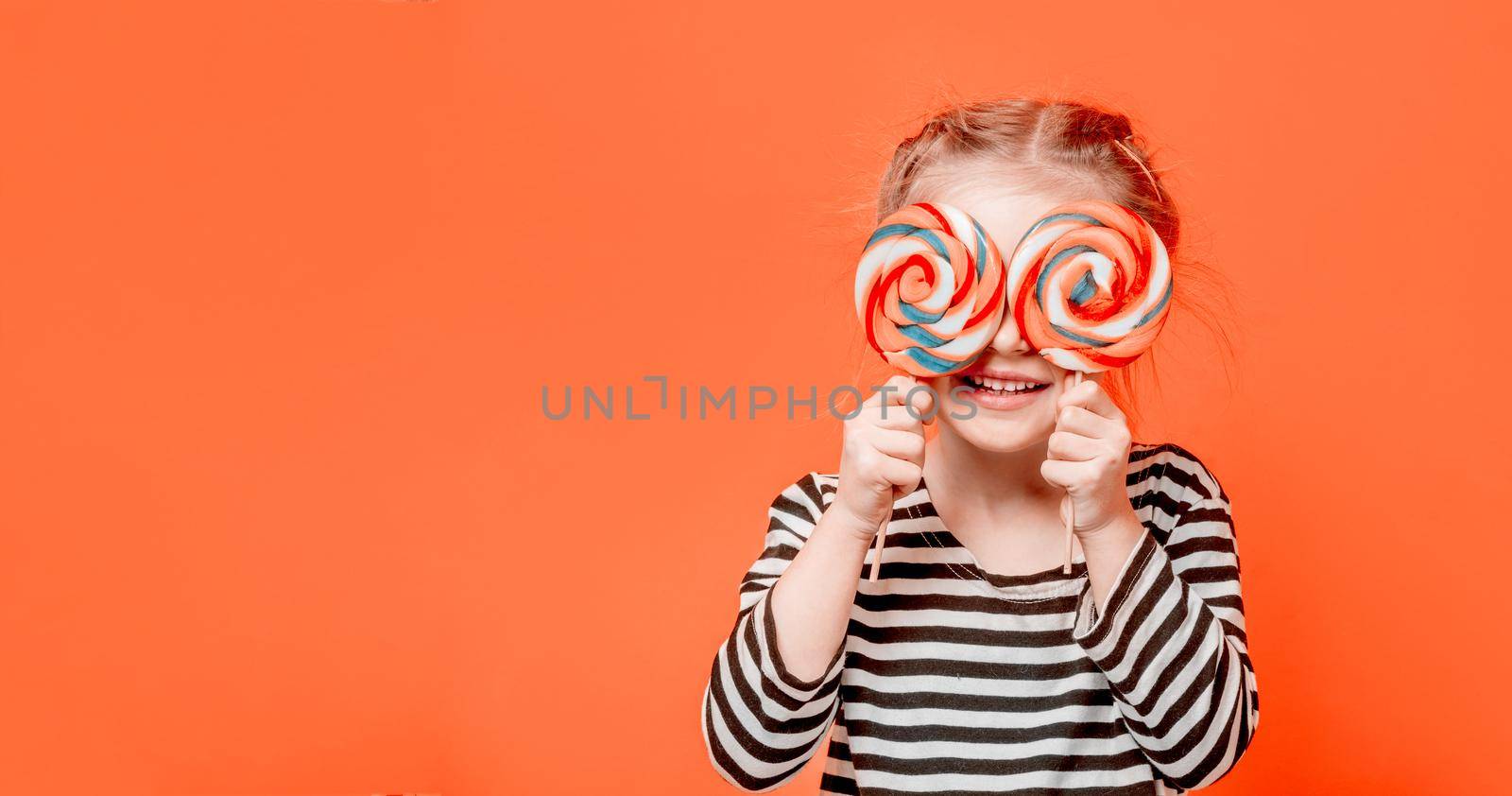 Cute kid girl holding two round colourful lollypops in front of her eyes