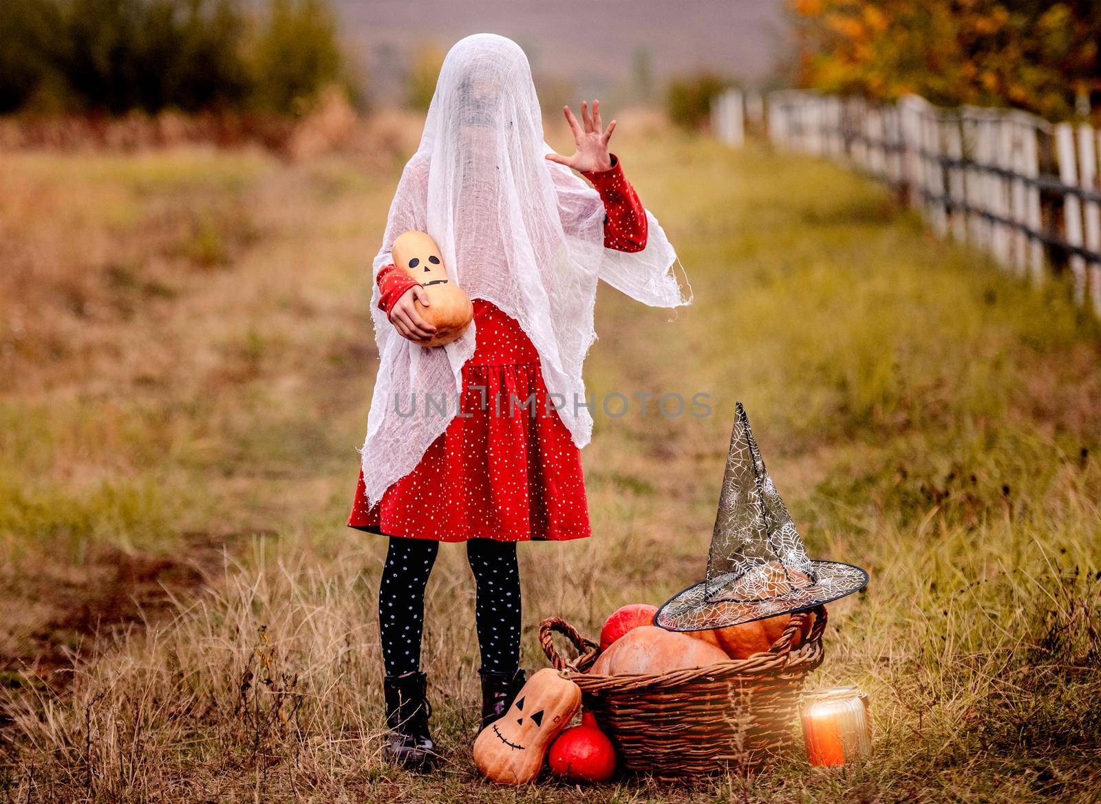 Little girl in halloween costume with pumpkin frighting on autumn nature background