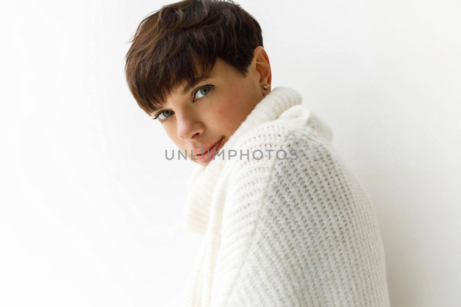 Portrait of young charming woman with short haircut posing in white sweater looking at camera.