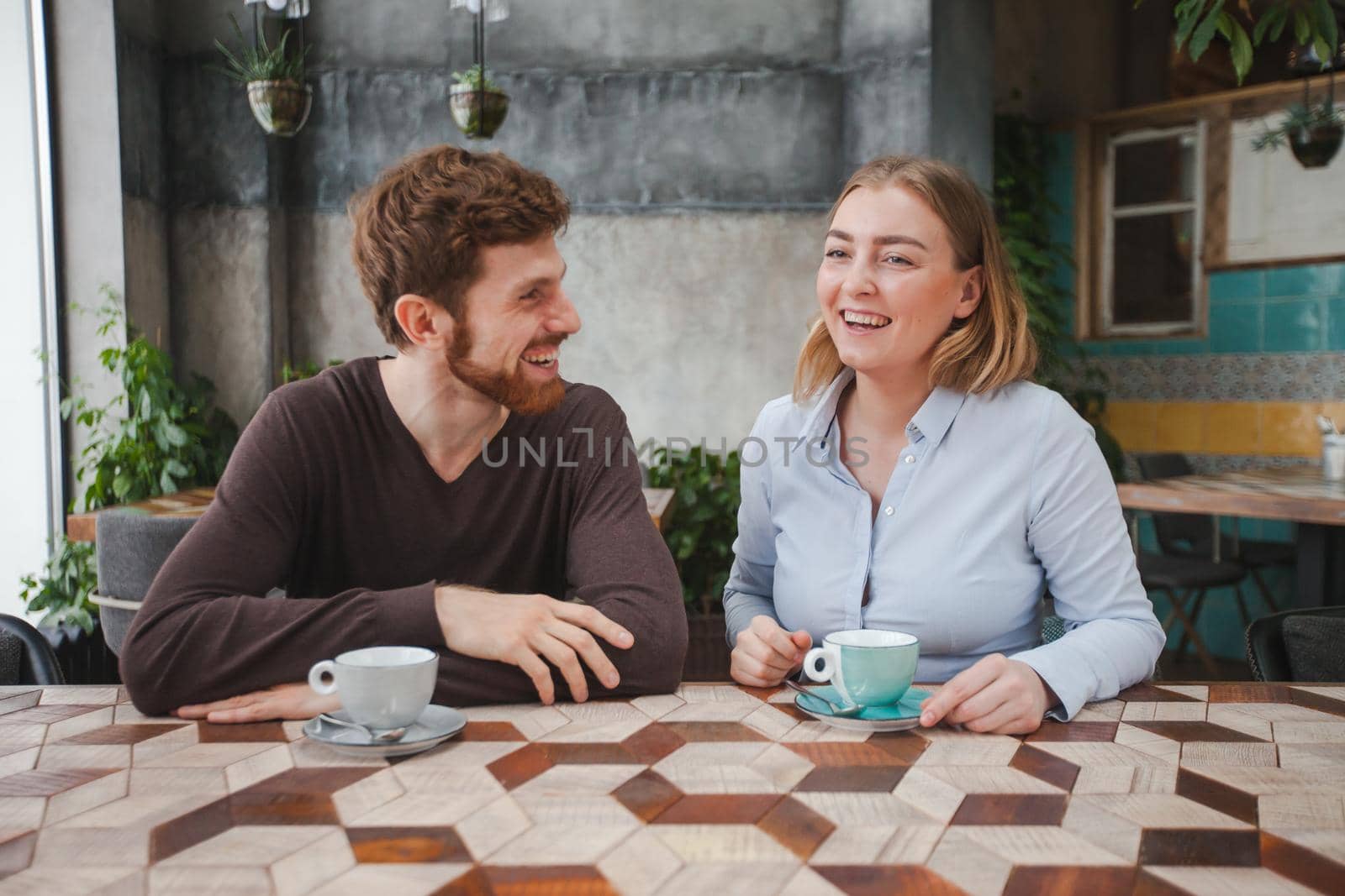 Cheerful young couple sitting on date in cafe and drinking coffee.