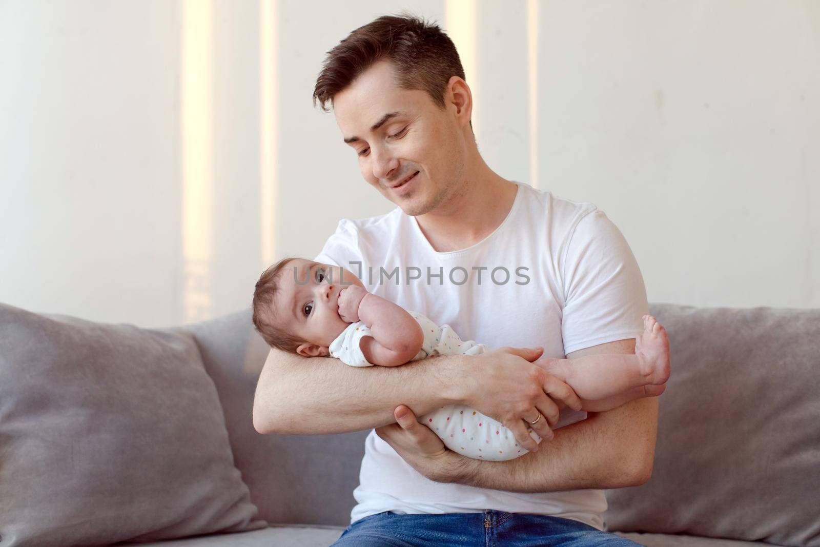 Young father sitting on sofa and holding baby on hands by Demkat