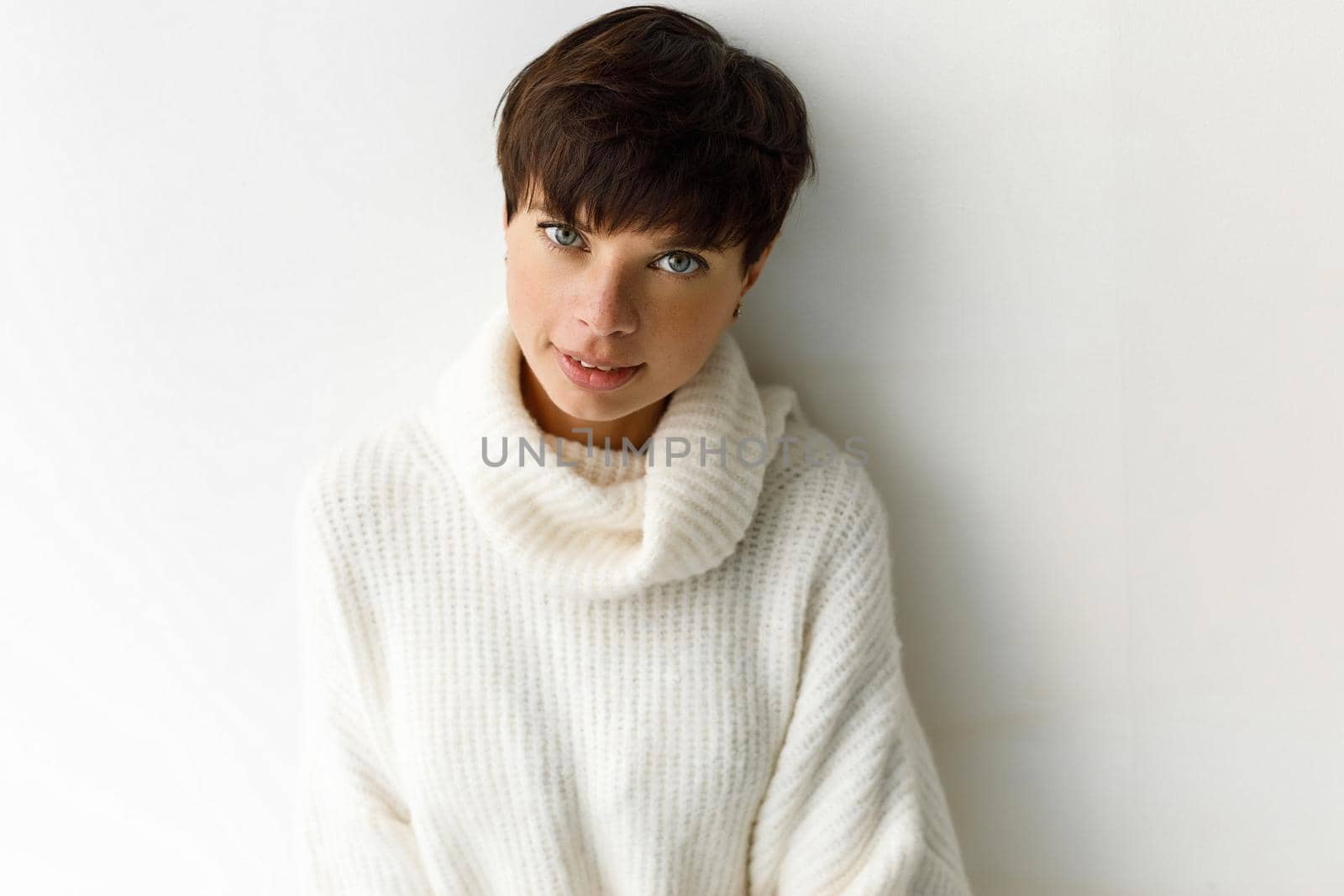 Portrait of young charming woman with short haircut posing in white sweater looking at camera.