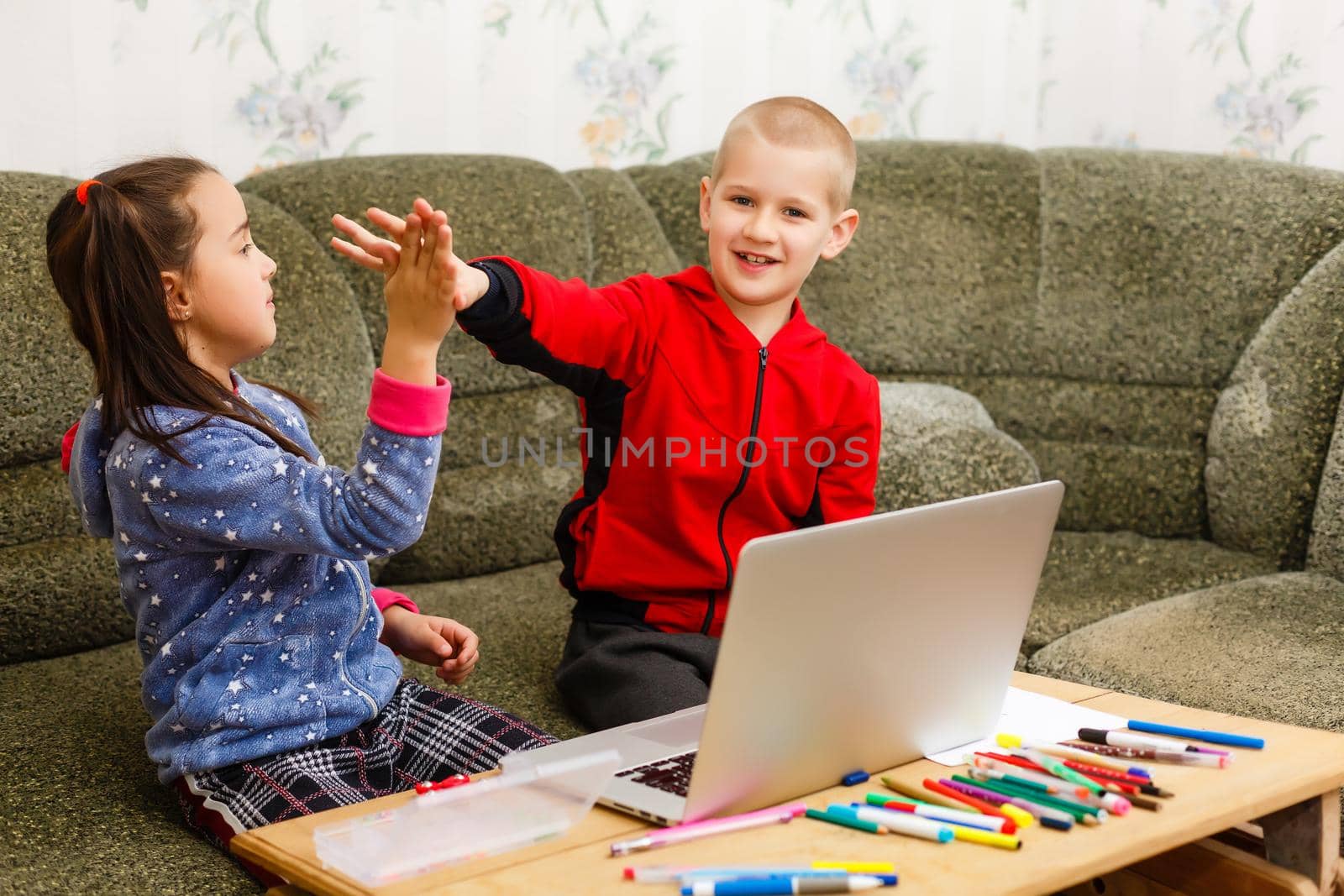 Two beautiful cute happy smiling children, a boy and a girl, use laptop for distance learning or entertainment.