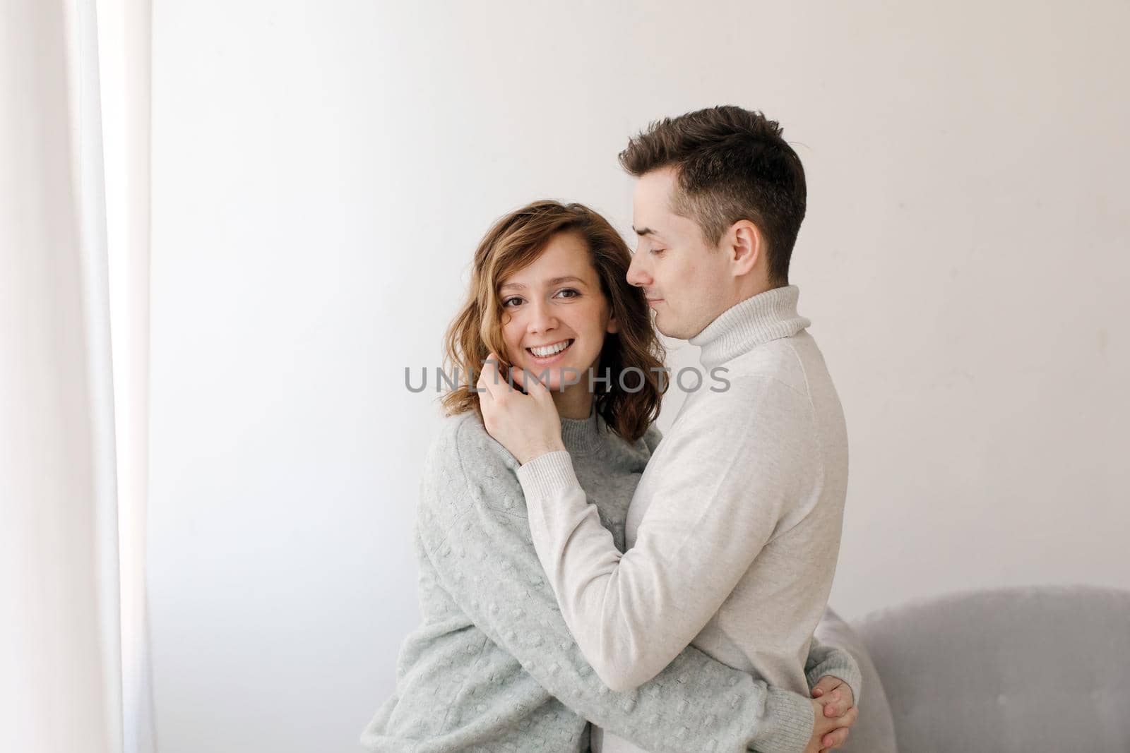 Embracing man and woman in sweaters standing in embracing at home being in love