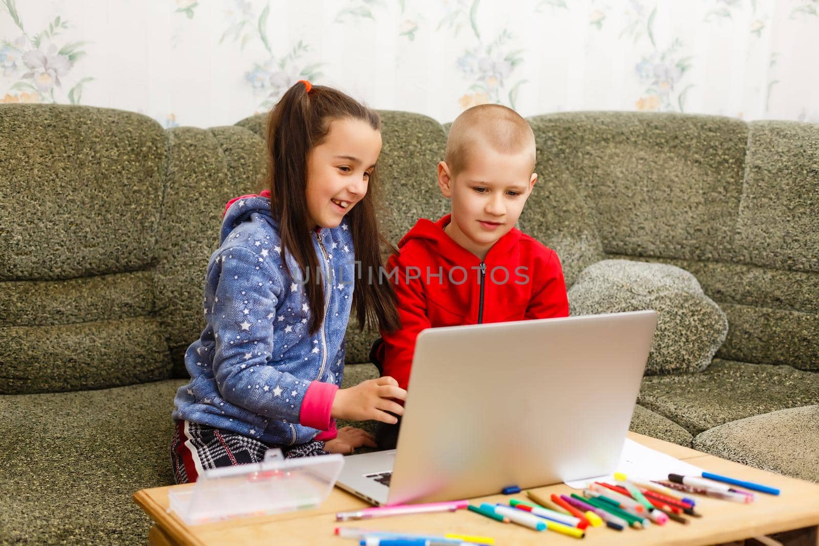 Two beautiful cute happy smiling children, a boy and a girl, use laptop for distance learning or entertainment. by Andelov13