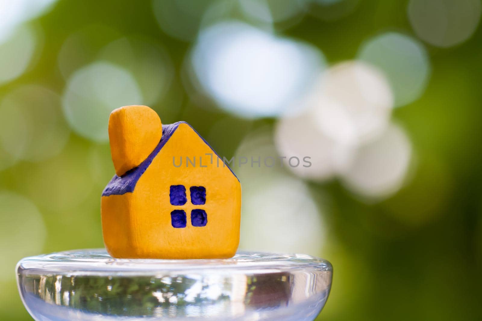 Miniature yellow toy house on a glass dais. Selective focus