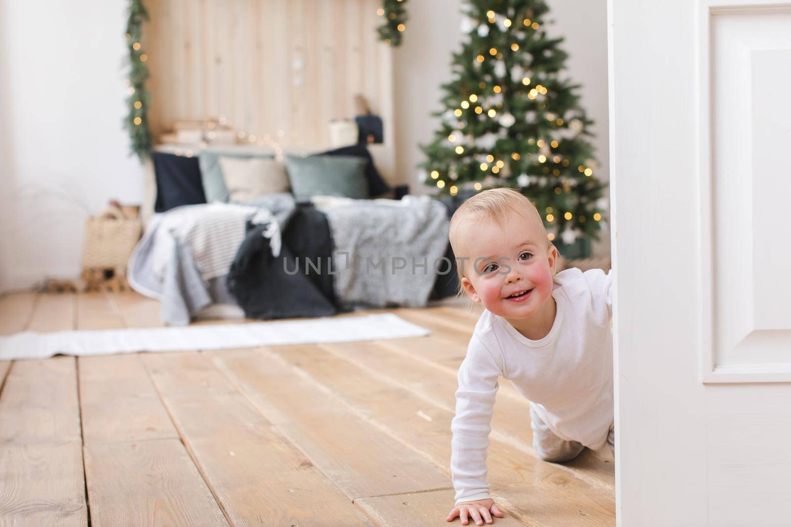 Adorable infant standing in doors on background of Christmas tree in bedroom