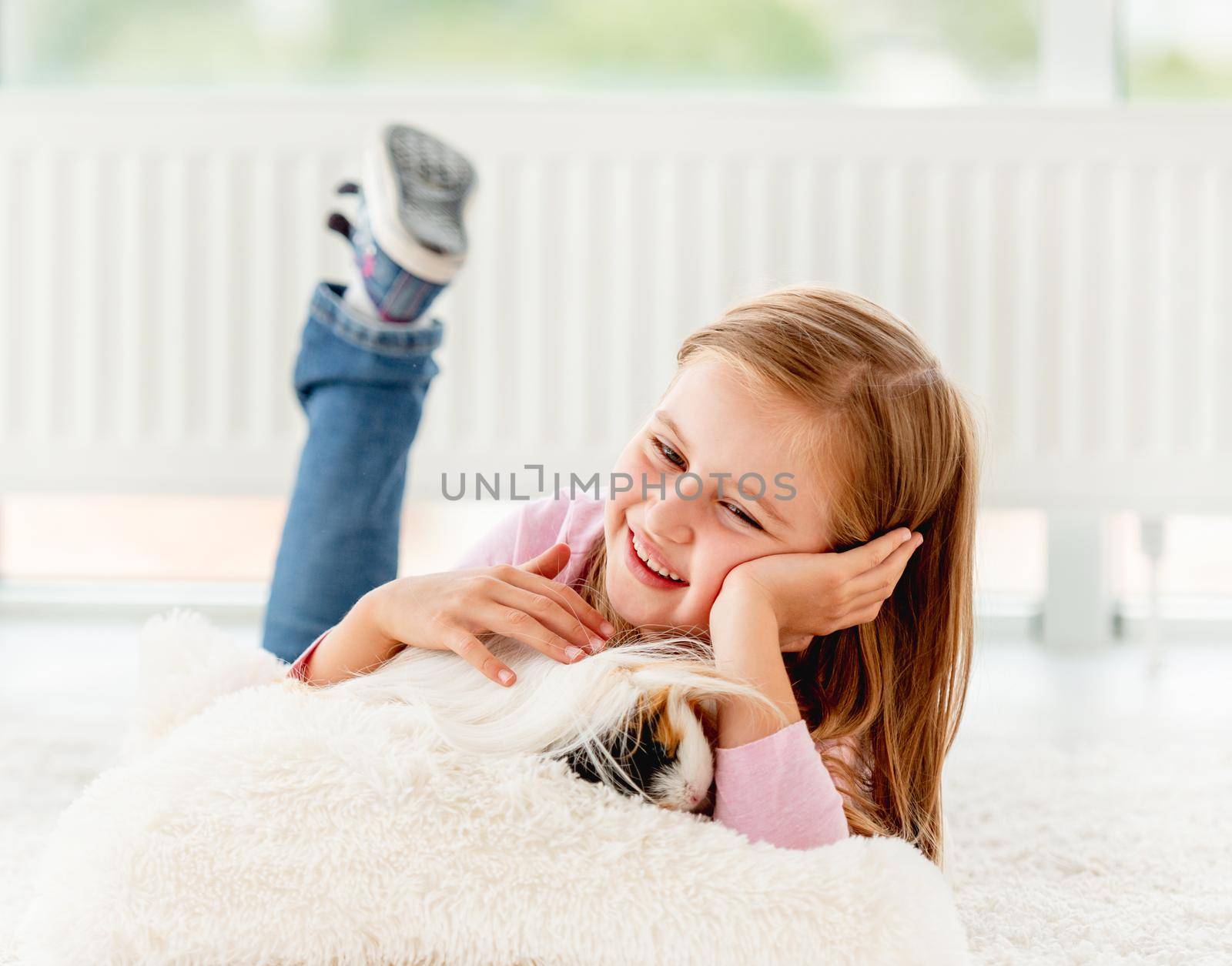 Lovely girl lying on the floor and gently holding hairy guinea pig in her hands