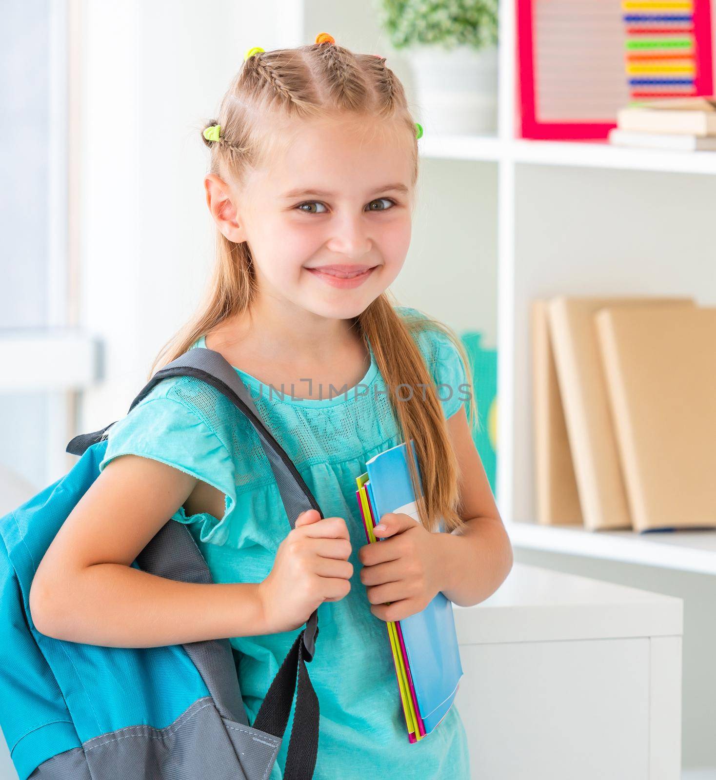 Smiling funny active little girl is ready for school again, holding new blue backpack and notebooks