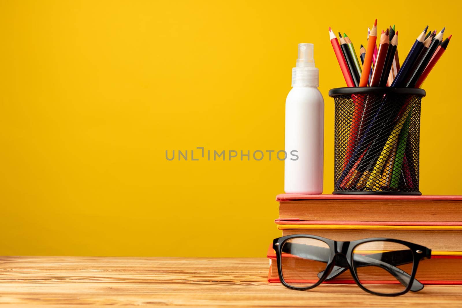 Back to school concept with stationery in cup and hand antiseptic spray against yellow background