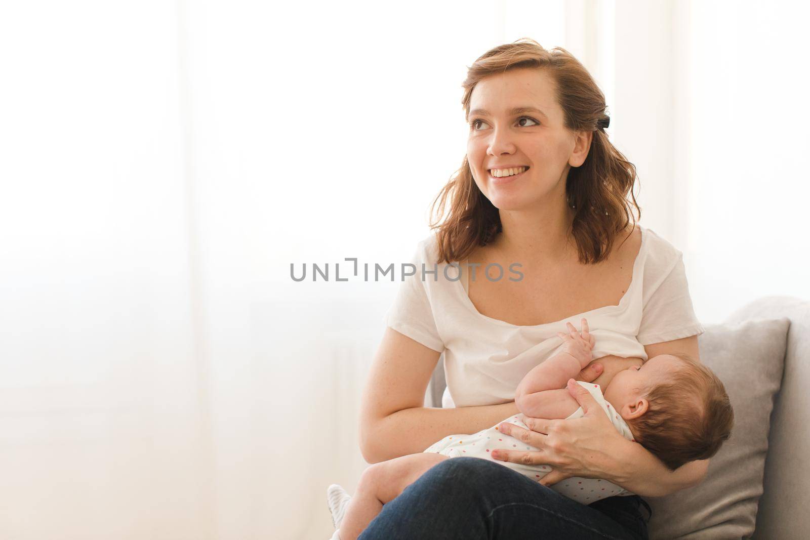 Cheerful young woman breastfeeding infant child at home.