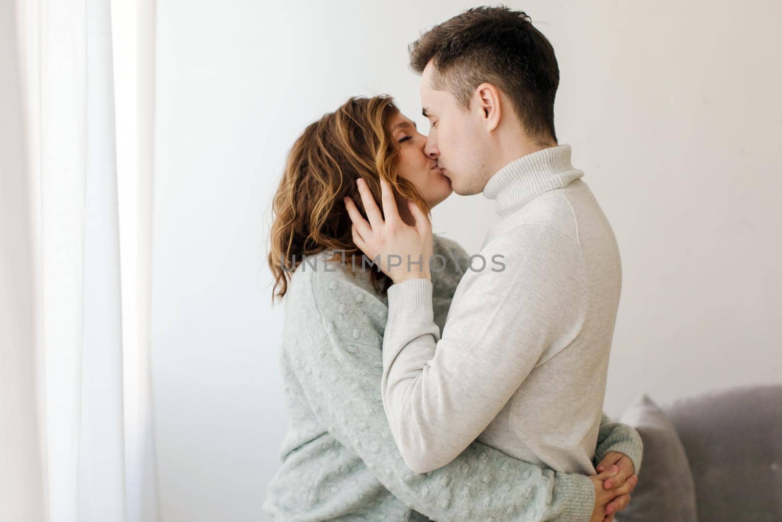 Side view of young man and woman standing and kissing at couch.