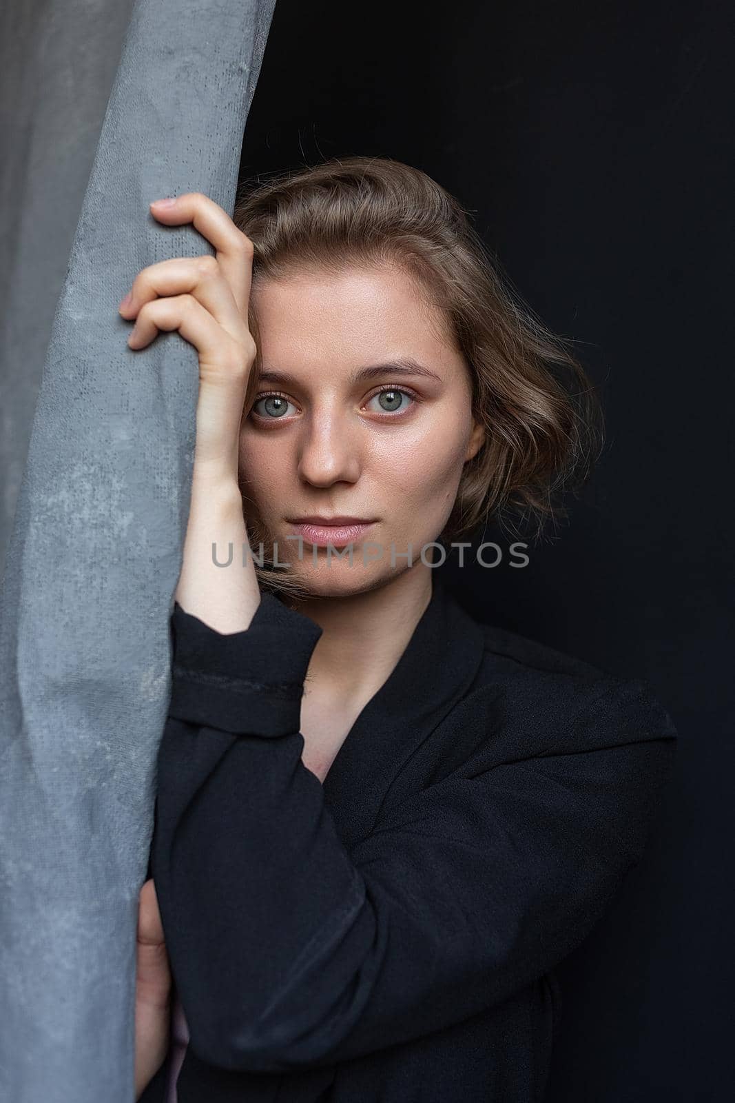portrait of young caucasian woman with short hair posing in black suit jacket, holding curtain. closeup shot of pretty girl. short-haired attractive female poses in studio