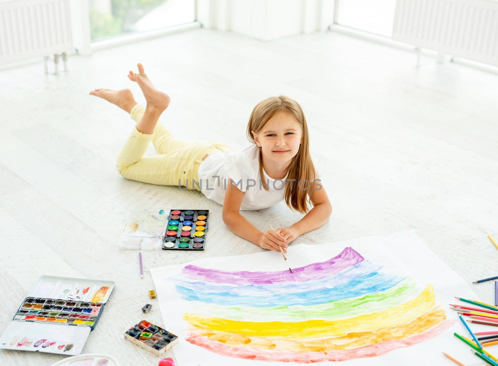 little cheerful girl draws lying on the floor