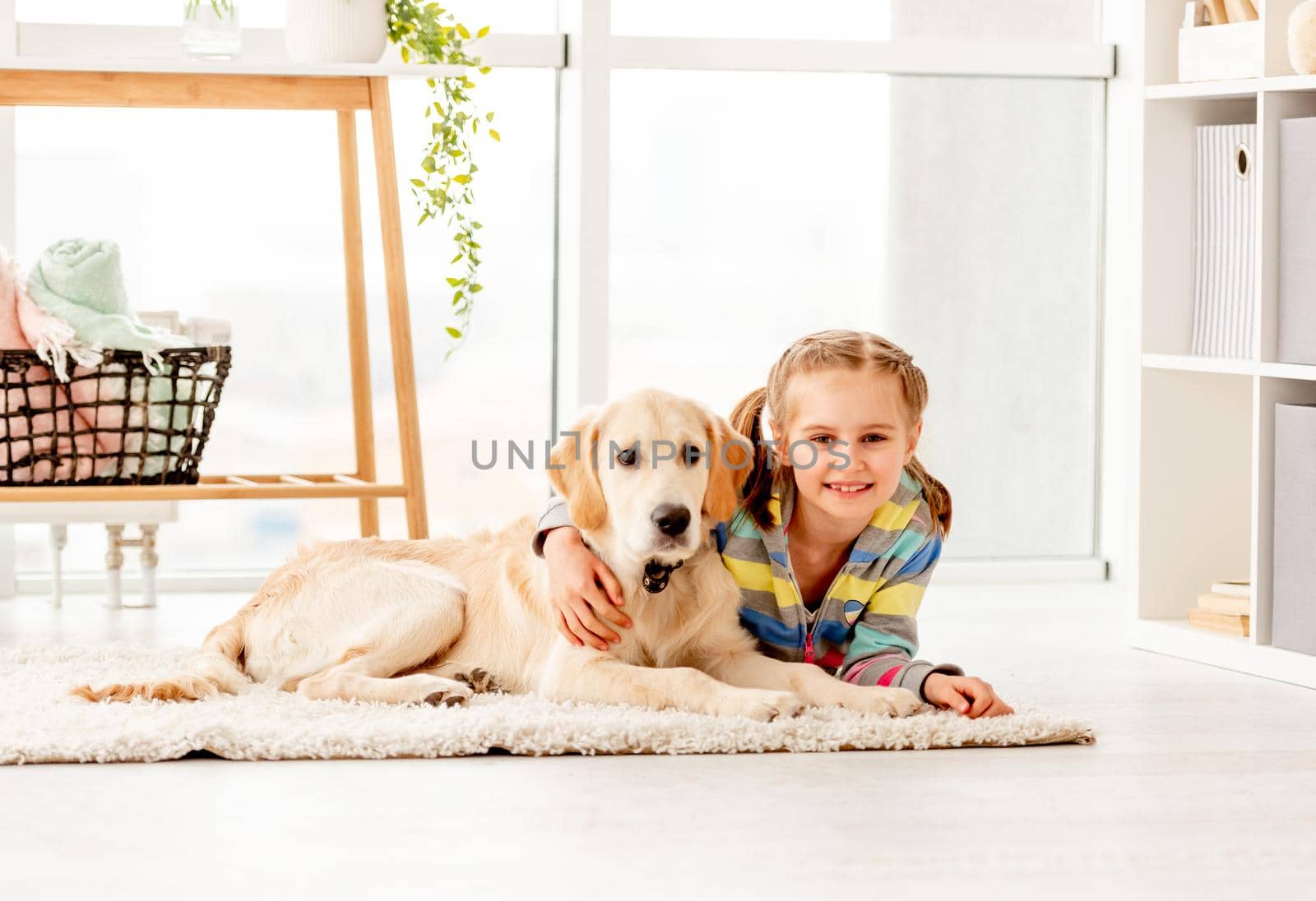 Happy school girl with calm young retriever dog lying at home