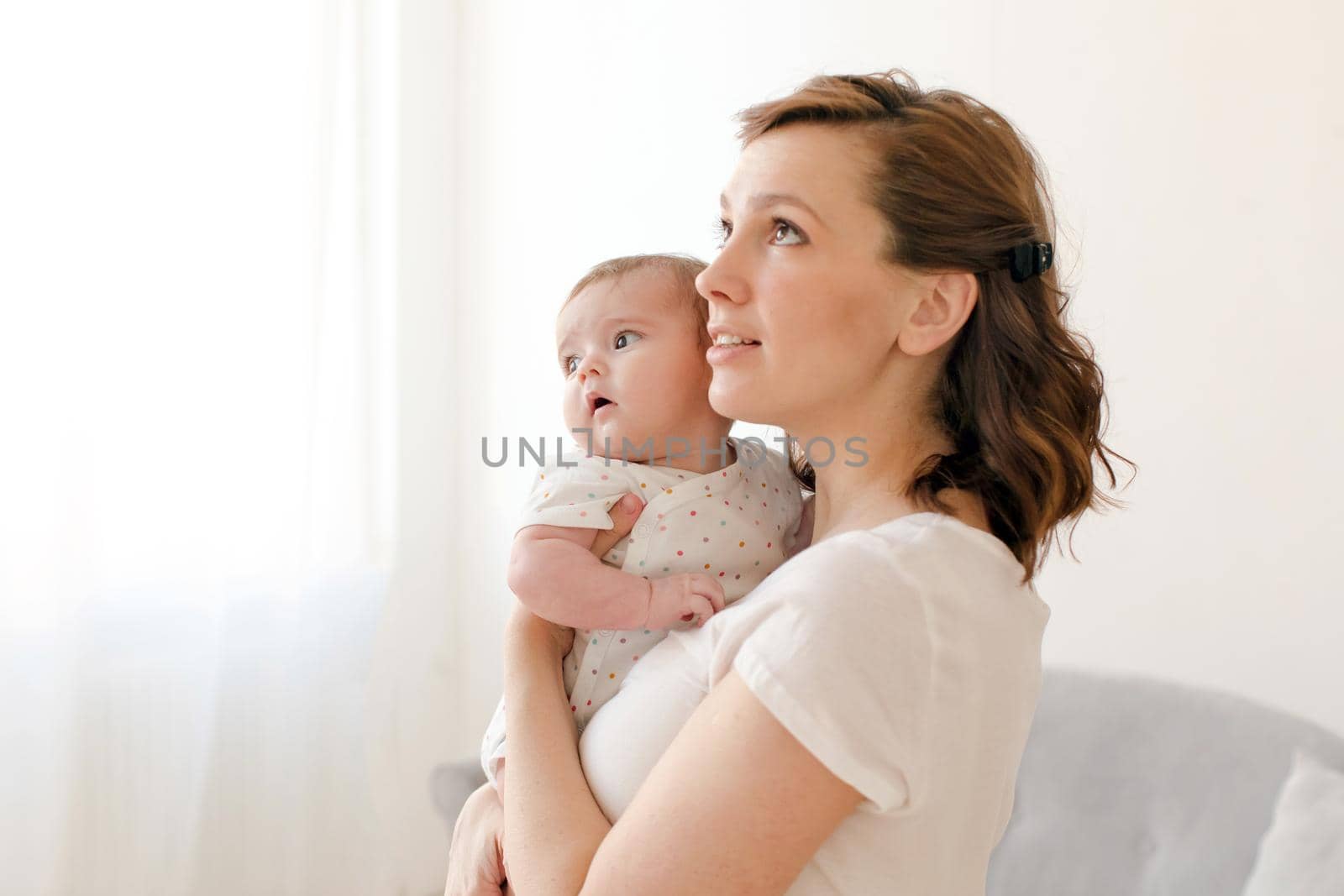 Beautiful young woman with baby on hands looking up while standing at home