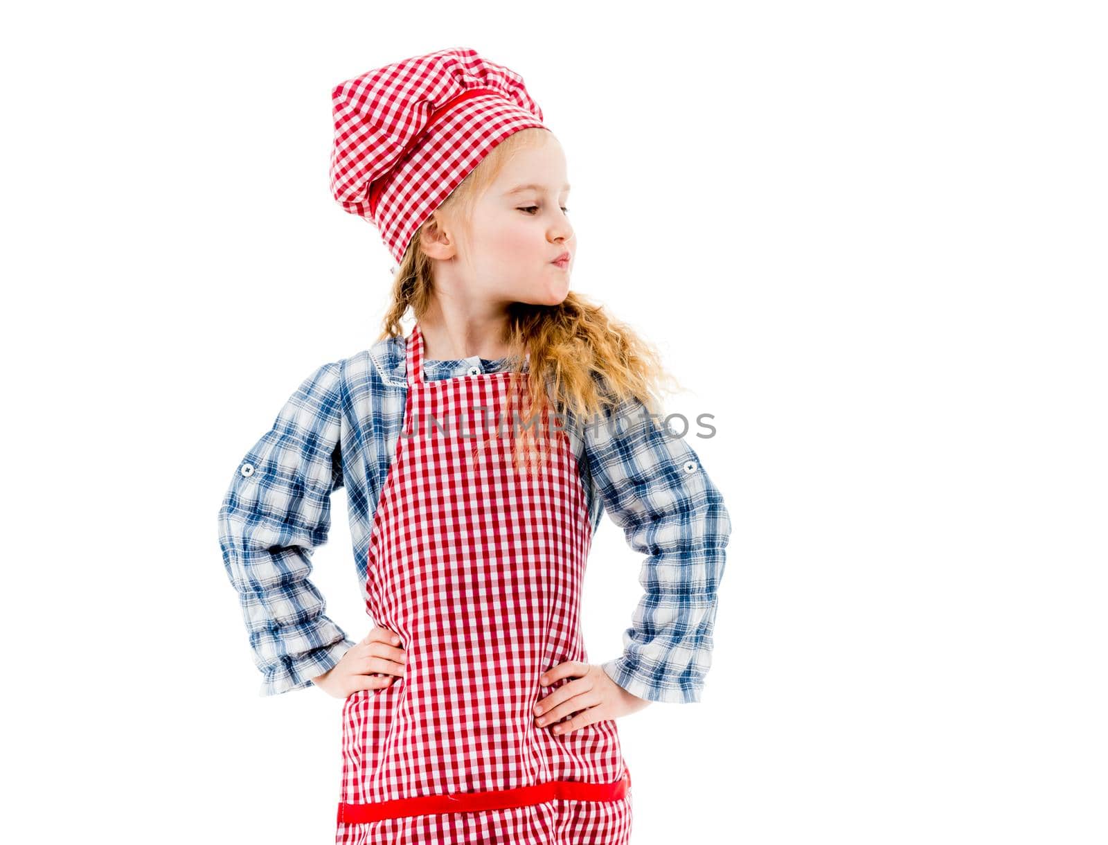 Little child girl in red plaid apron standing in akimbo pose isolated on white background