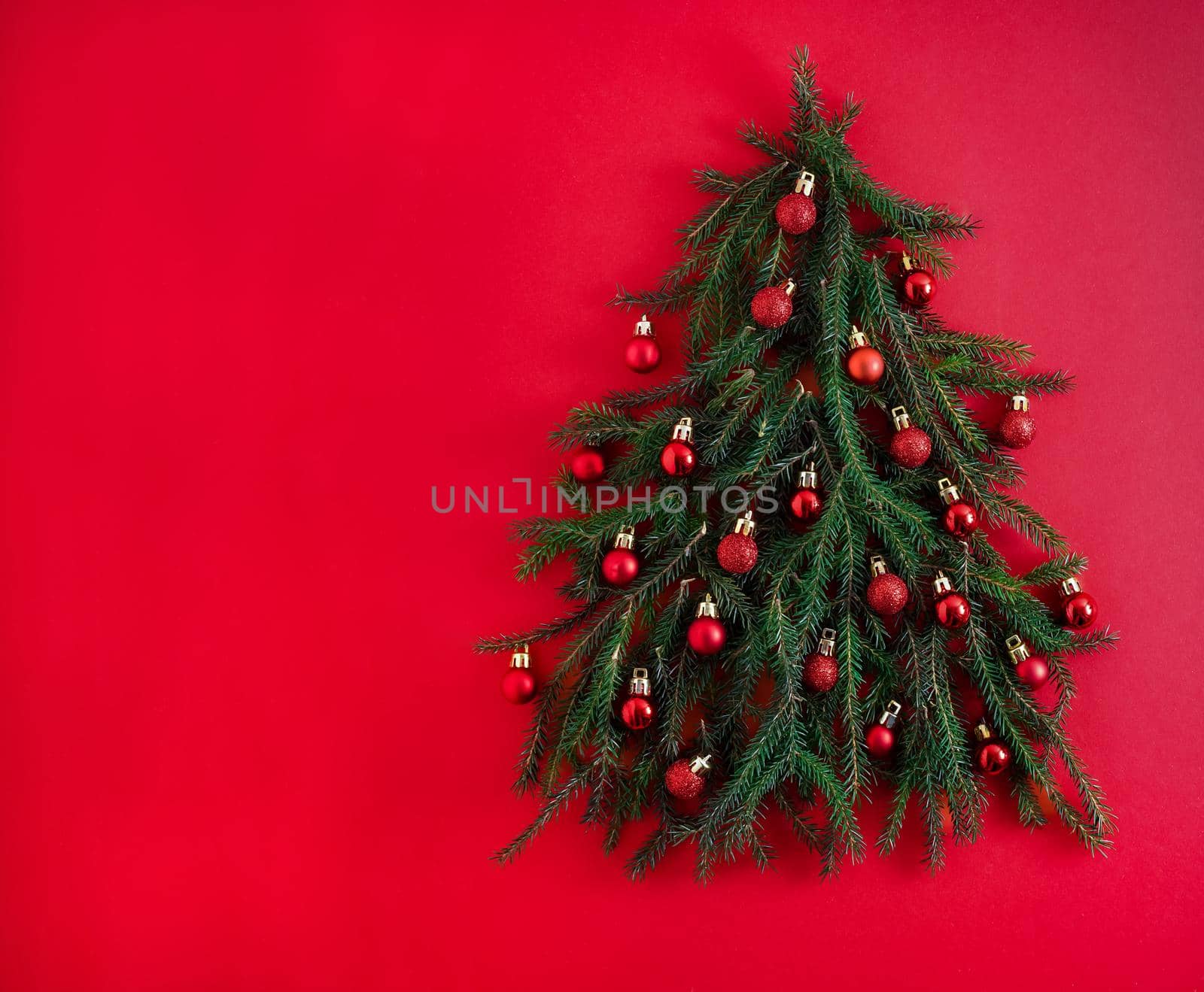 Christmas tree made of green coniferous branches on a red background. Christmas background with place for text. Christmas holiday concept. Ball toys. Copy space.