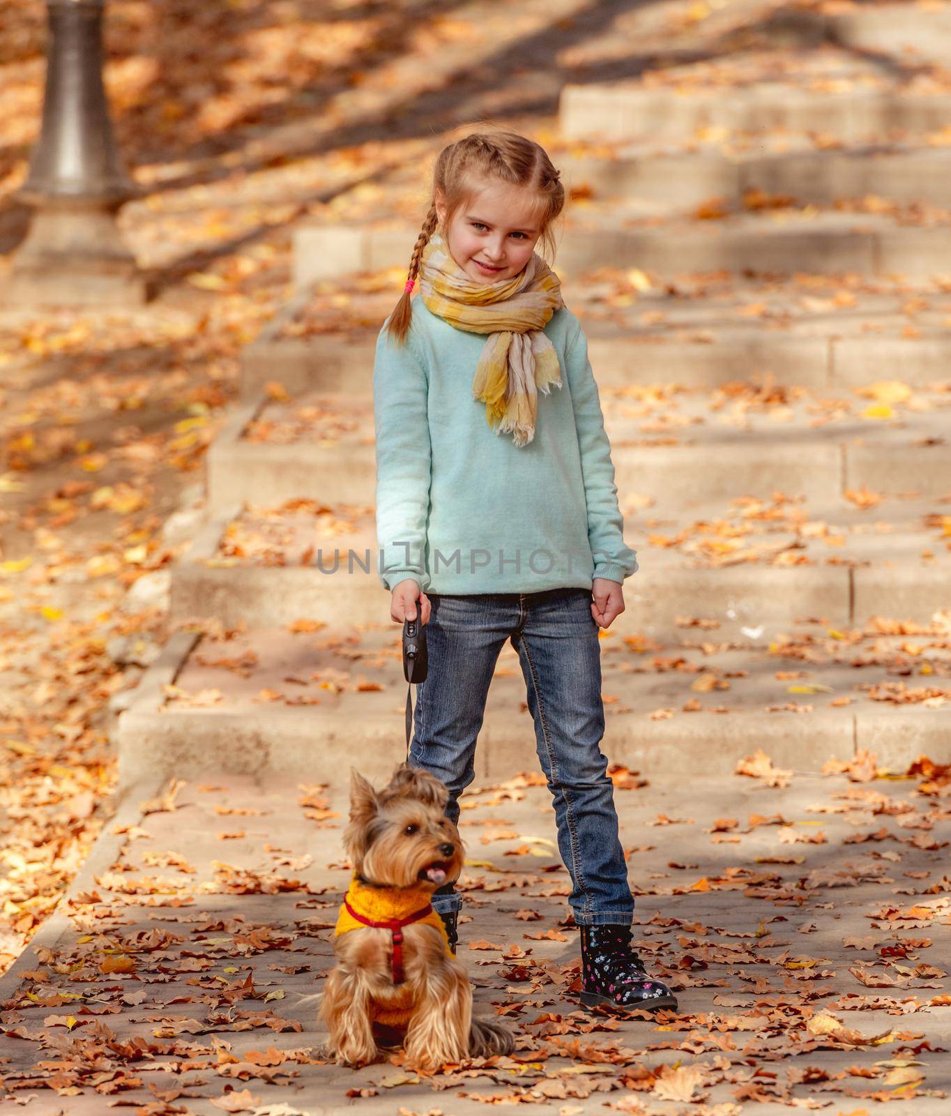 Cute little girl with yorkshire terrier in autumn park