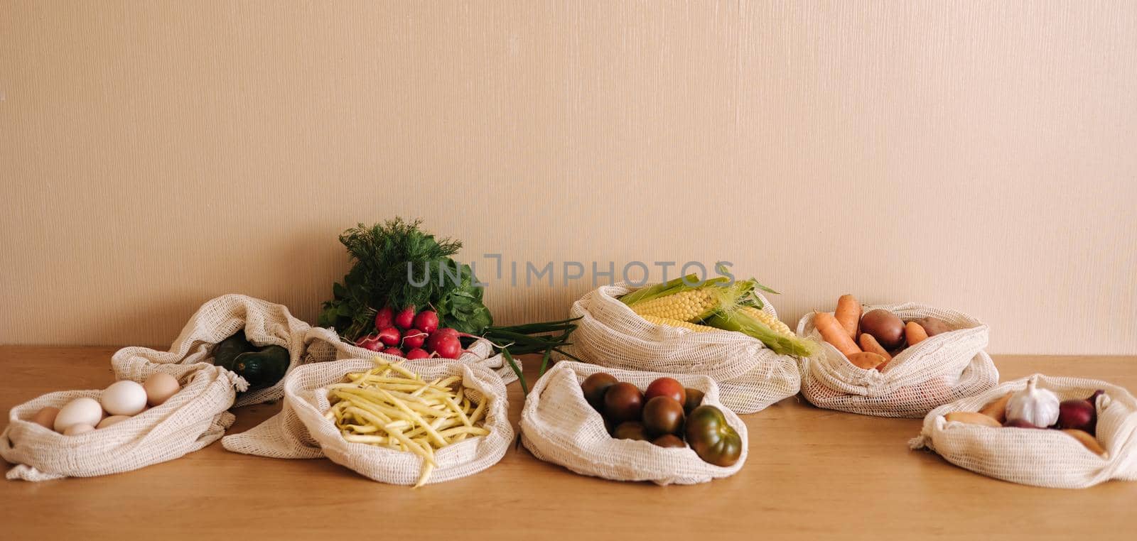 Vegetables in reusable eco cotton bags on wooden table. Zero waste shopping concept. Canvas grocery bag with tomatoes, carrot, potato. Plastic free items.