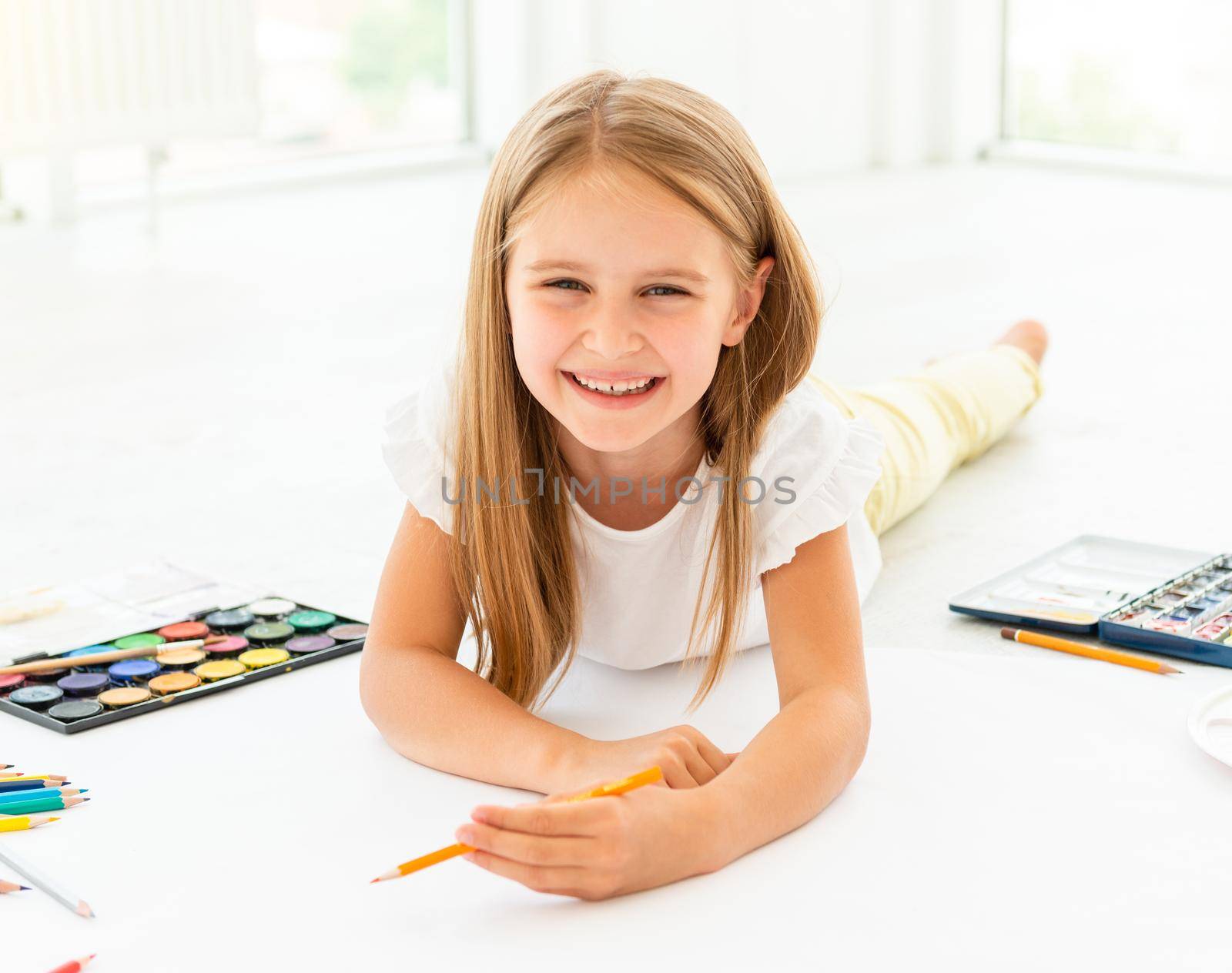 little cheerful girl draws lying on the floor