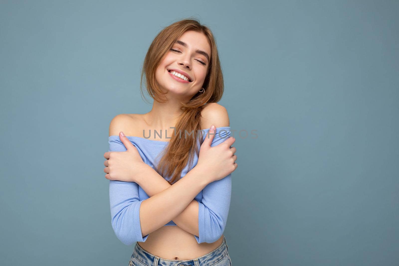 Smiling young positive beautiful dark blonde woman with sincere emotions isolated on background wall with copy space wearing casual blue crop top. Happy concept by TRMK