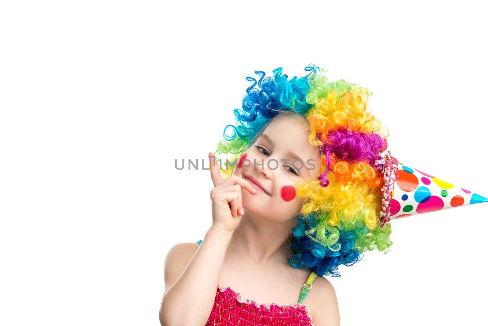 Funny little girl in multicolored clown wig pointing up on blank space, isolated on a white background, space for text
