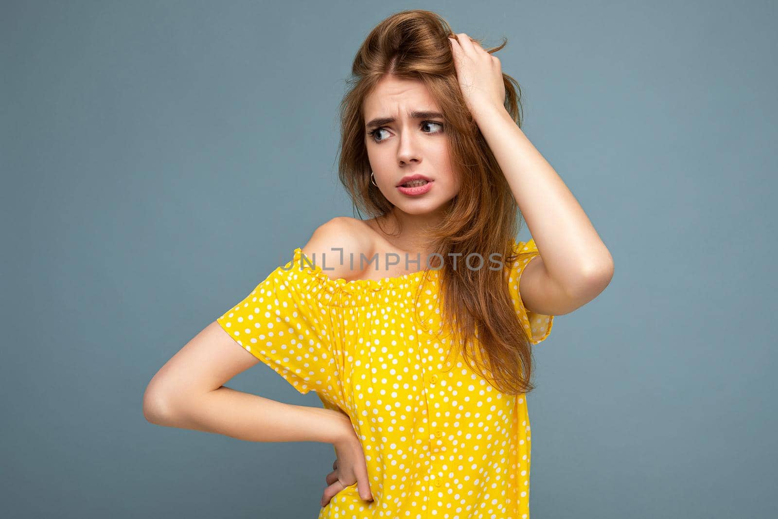 Young sad upset beautiful dark blonde woman with sincere emotions isolated on background wall with copy space wearing stylish summer yellow dress. Sorrowful concept by TRMK