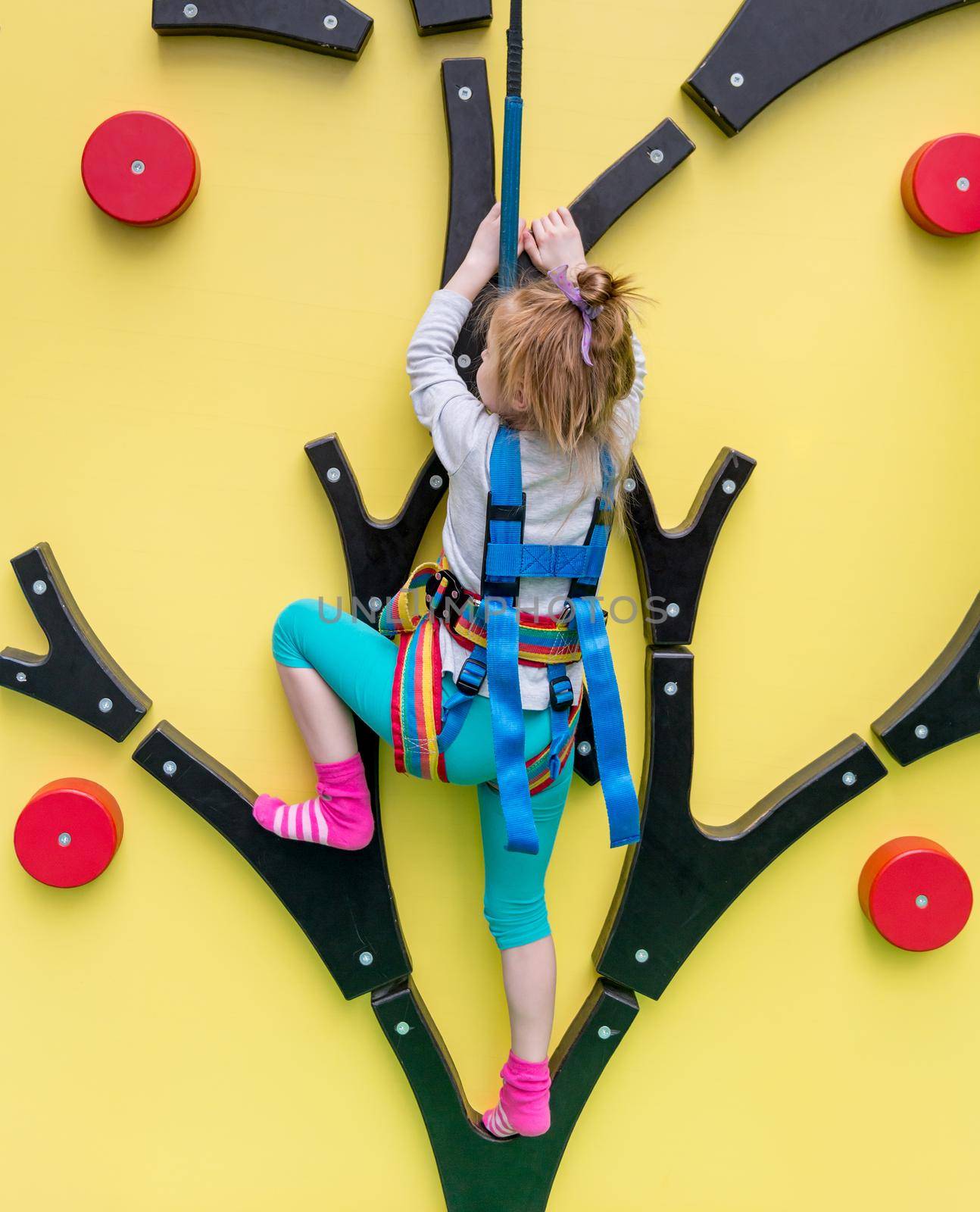 Little girl in insurance trains on climbing wall in indoor gym