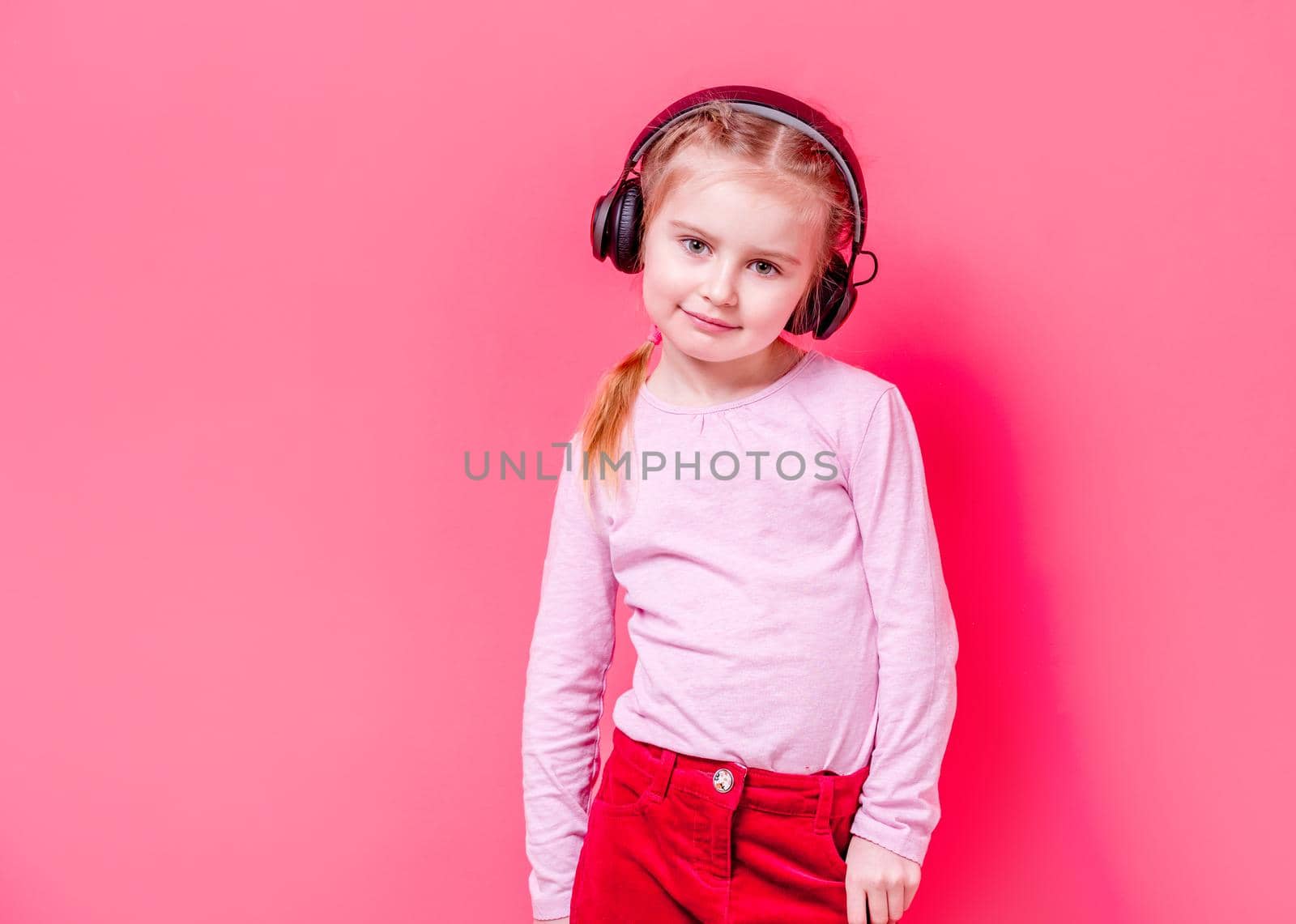Modern little girl posing in headphones over rose background