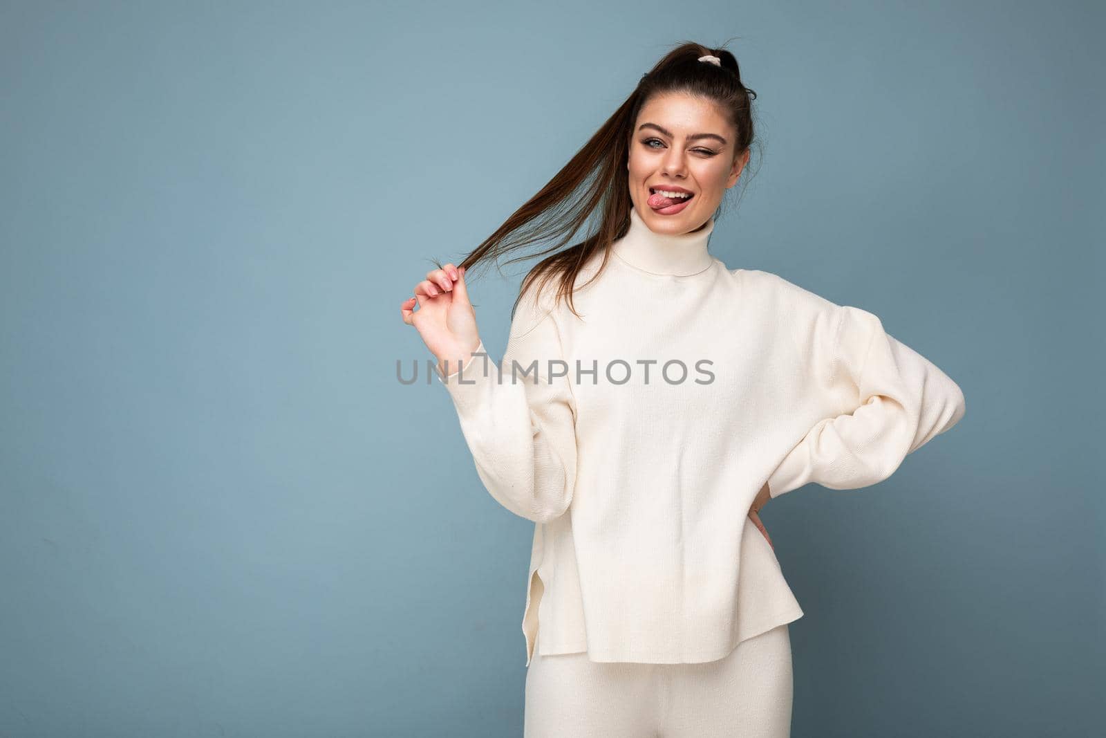 Young pretty european fashion brunette woman wearing casual white sweater isolated on blue background with sincere positive emotional expression on face by TRMK