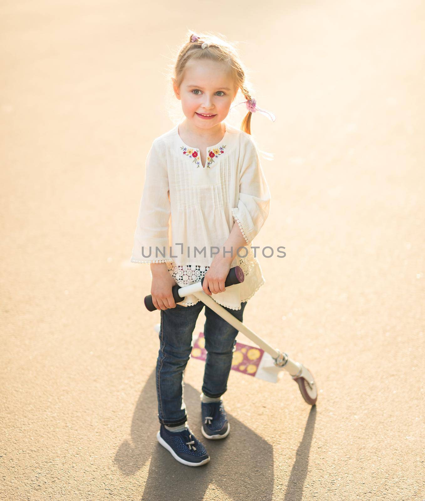 little girl wearning light linen white shirt with embroidery playing with her kick scooter