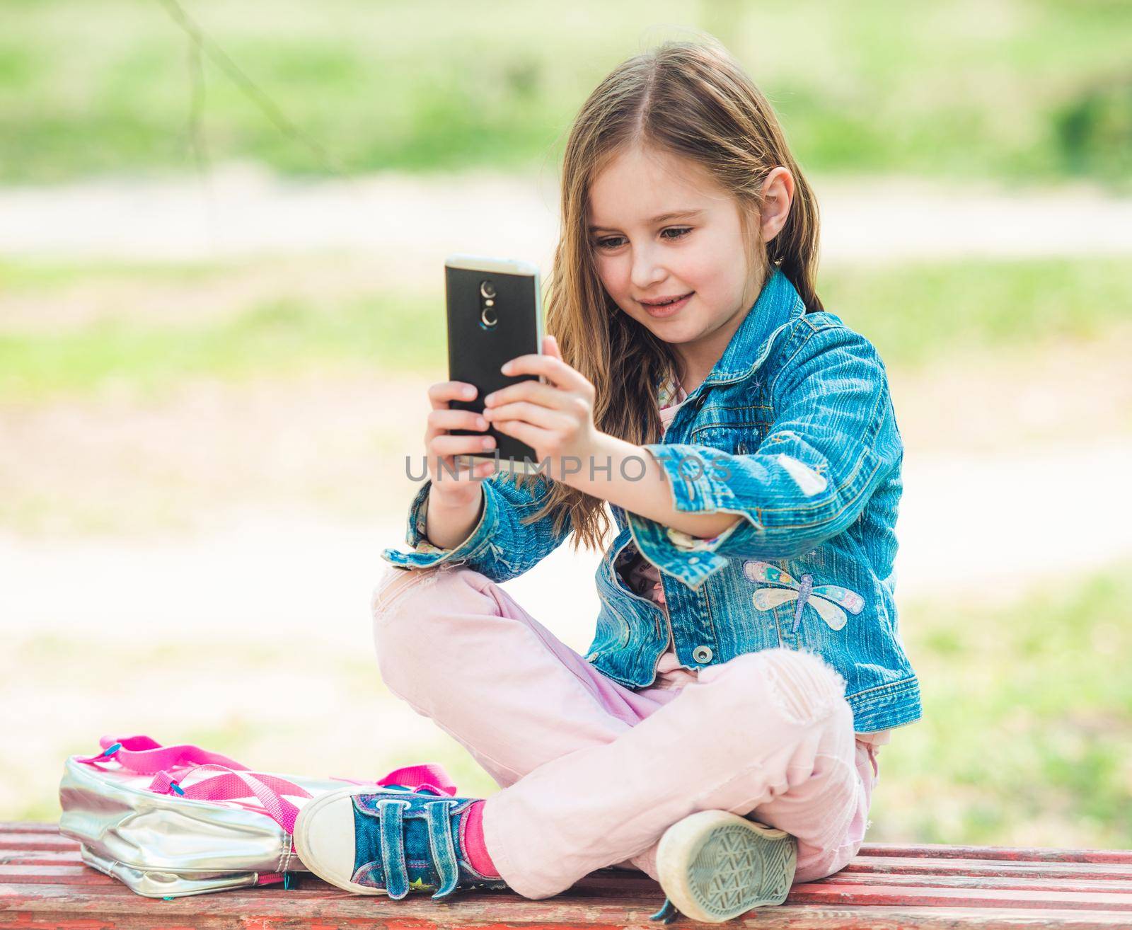 Pretty little preteen girl taking selfie in calm atmosphere of city park