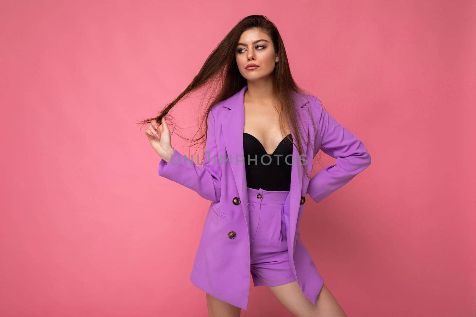 Portrait of young sexy cool attractive fashionable brunette woman wearing stylish violet suit isolated on pink background with empty space. Business concept.