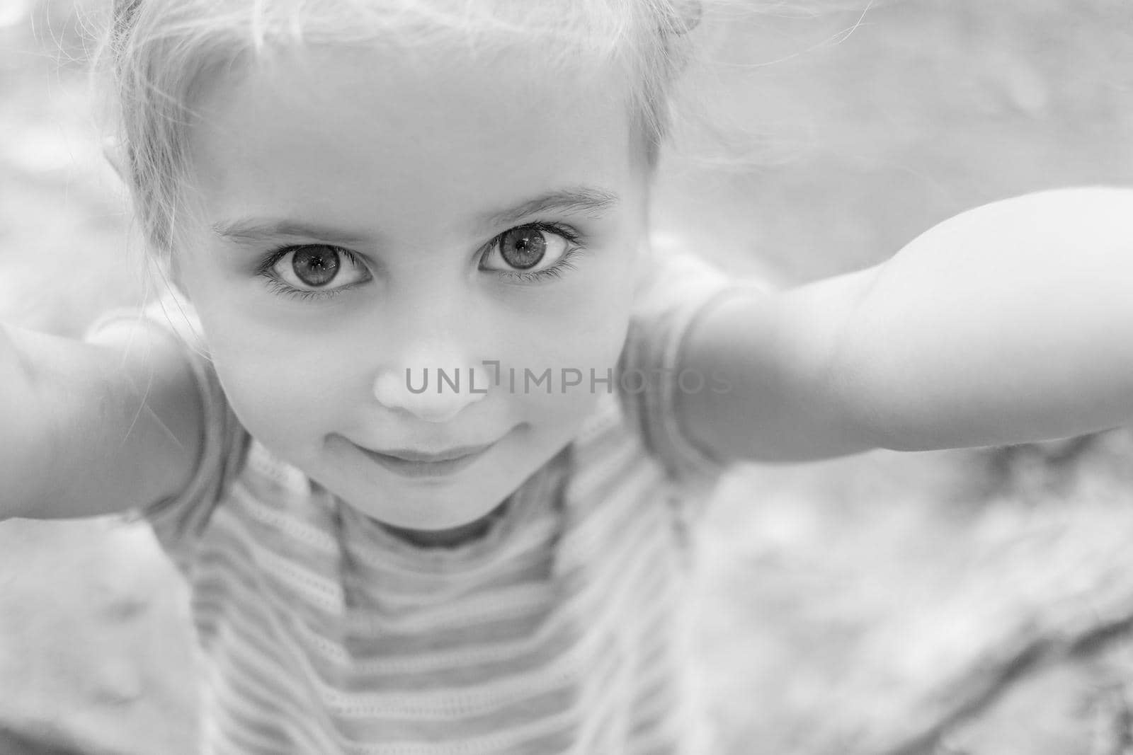 Cute little girl with big eyes smiles making selfie, black and white photo.