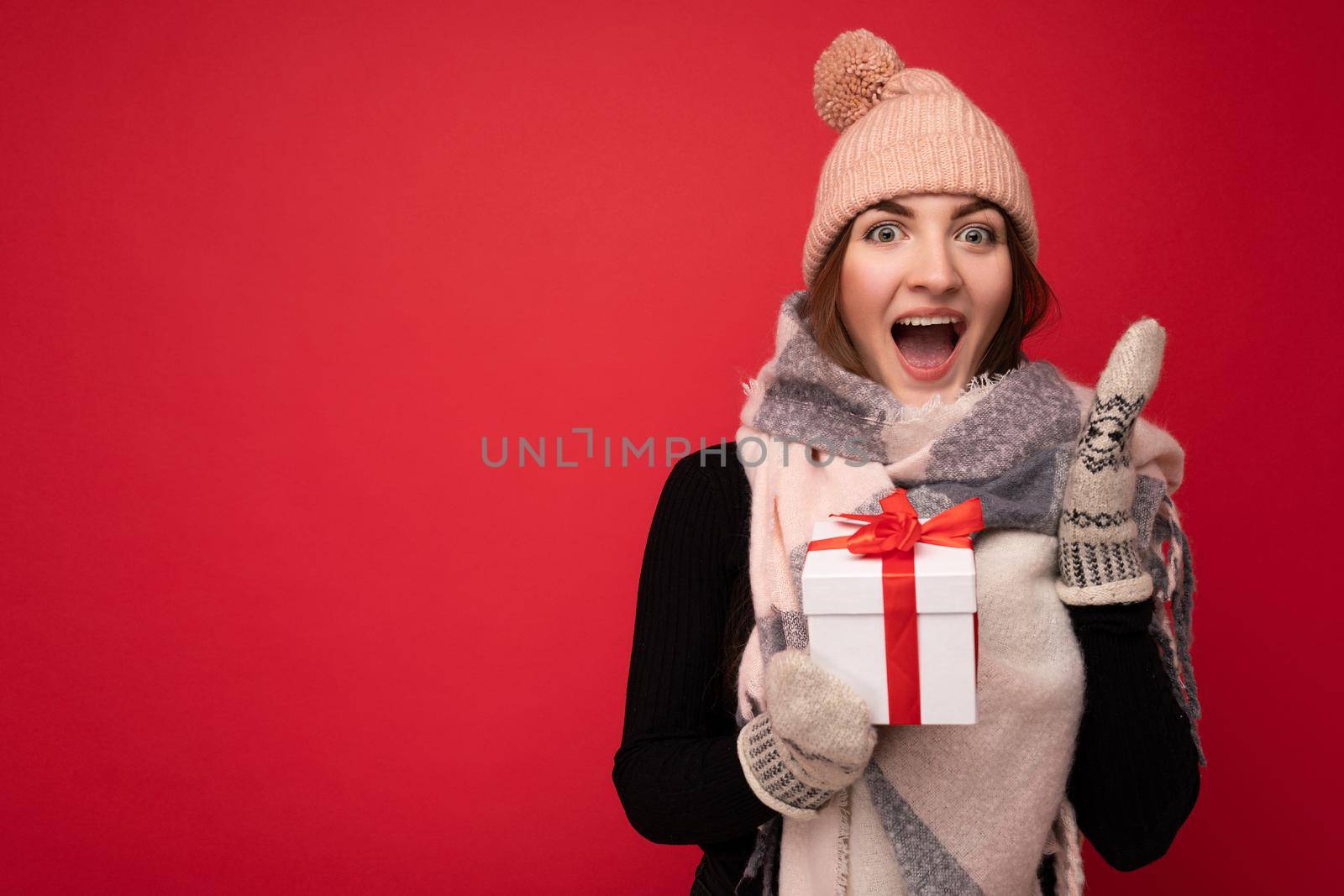 Photo shot of pretty positive surprised young brunet woman isolated over colourful background wall wearing trendy outfit look holding gift box and looking at camera. Free space