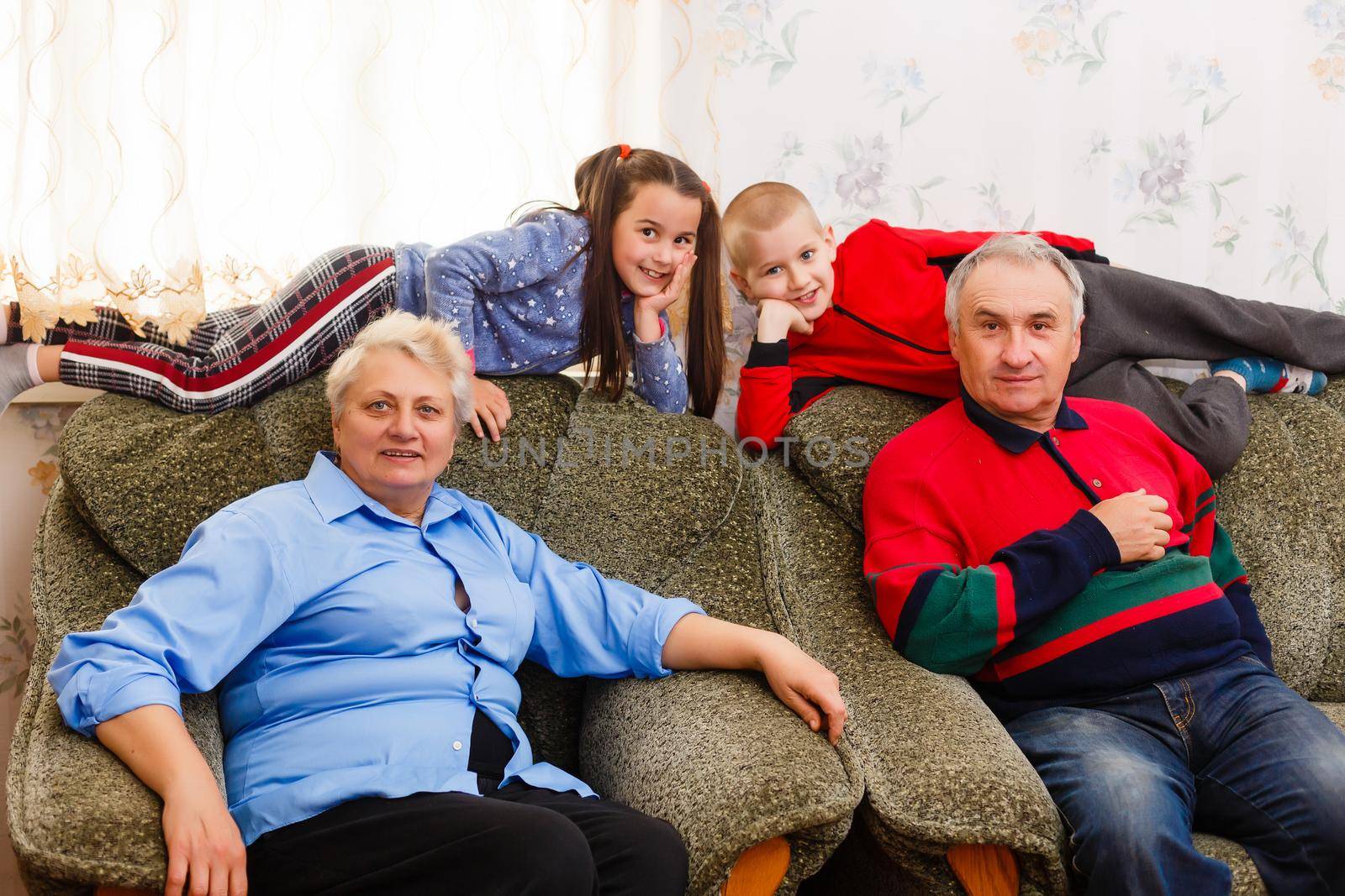 Happy young boy and girl with their laughing grandparents smiling at the camera as they pose together indoors by Andelov13