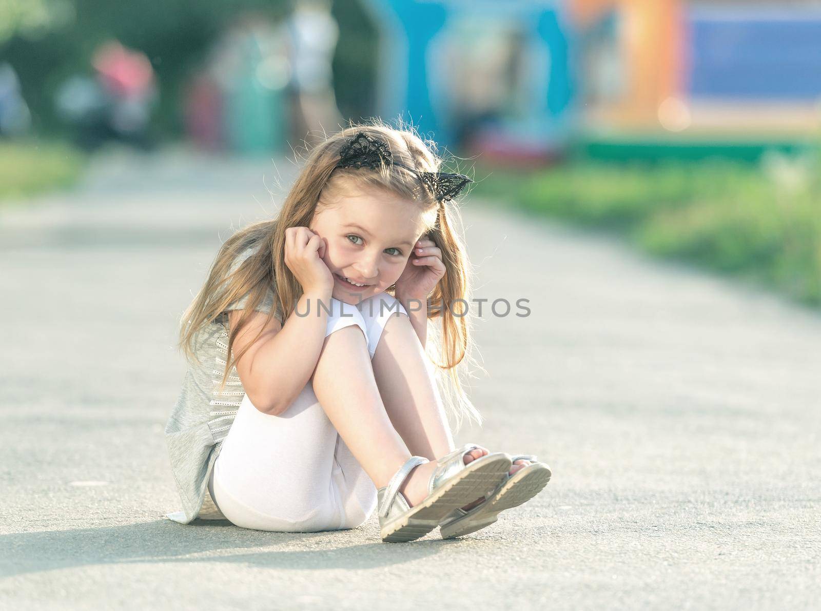 Little happy girl is sitting on the street