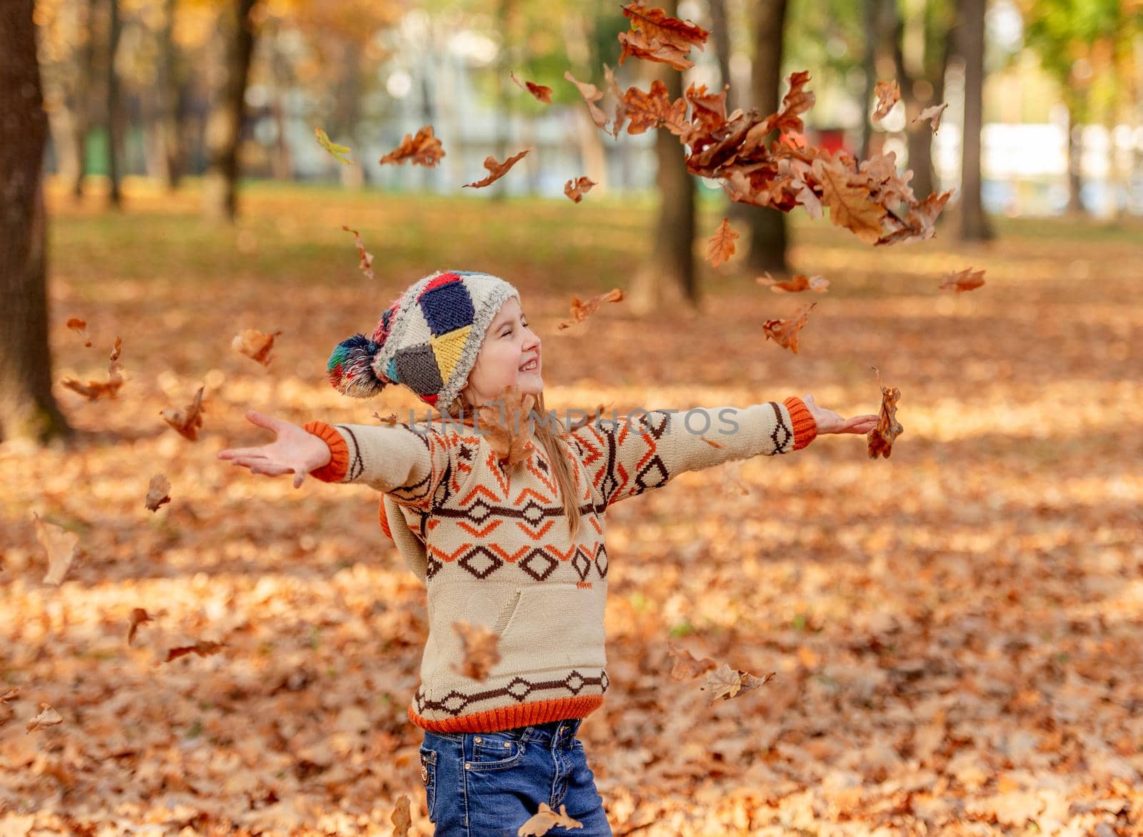 Cute little girl throwing up autumn leaves in park
