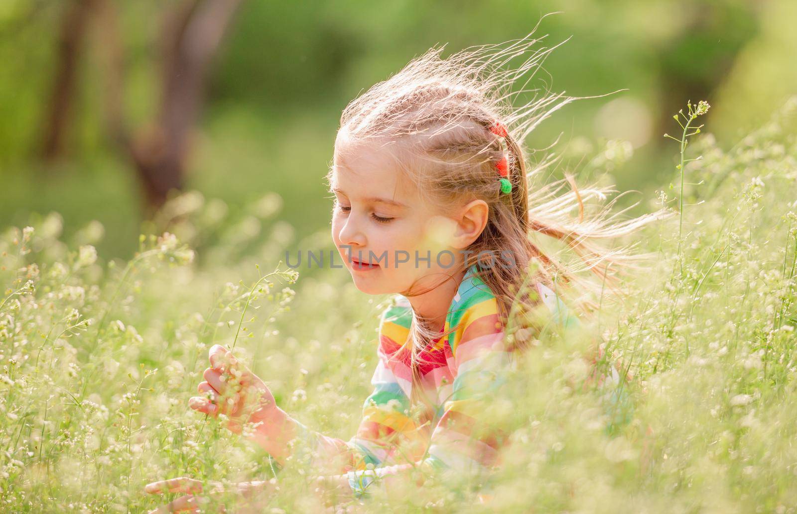 Kid girl with meadow flowers in summer windy sunny day
