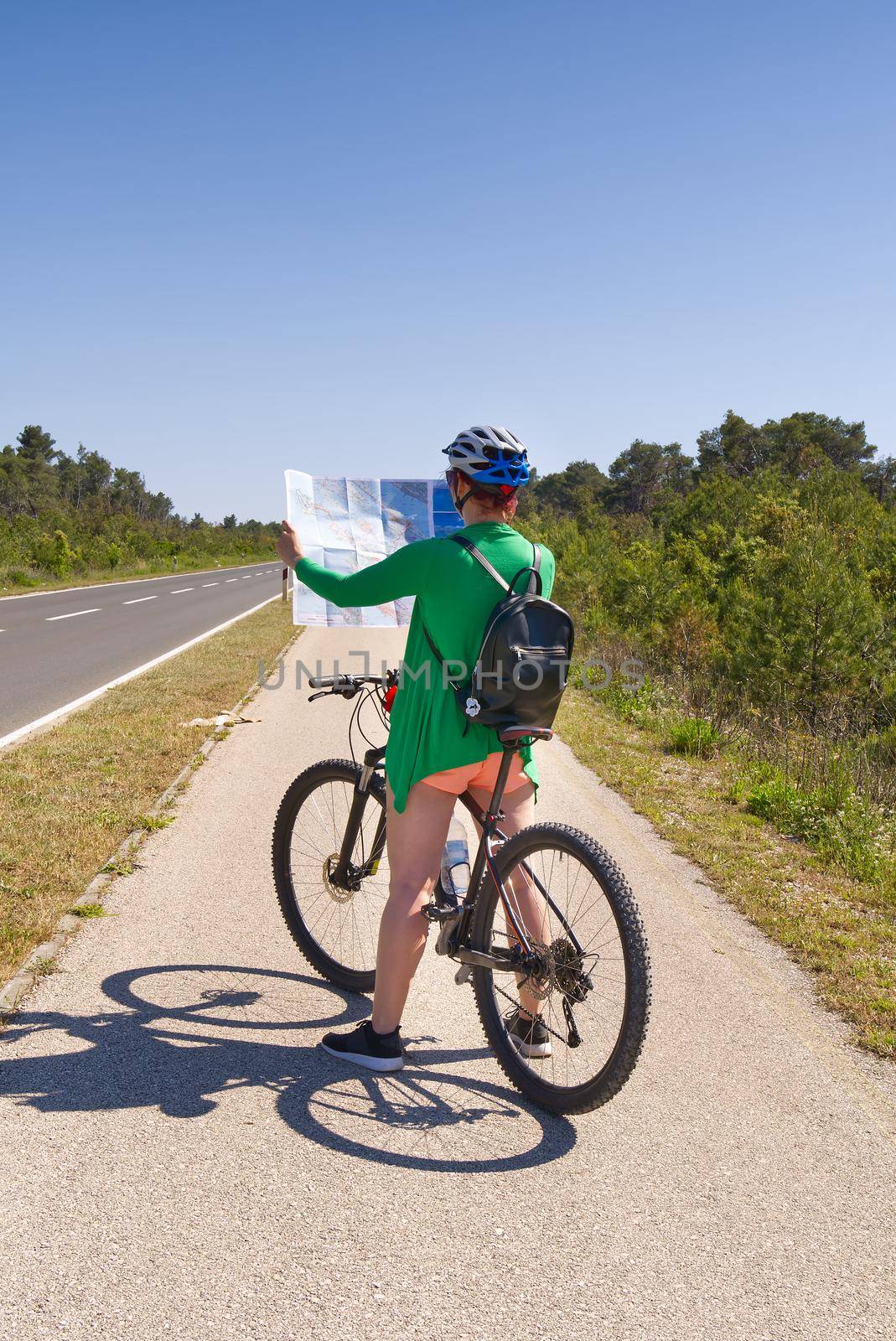 tourist, happy woman in a helmet on a bicycle examining a map at the intersection of bicycle roads. concept of outdoor activities or cycling travel in sunny day